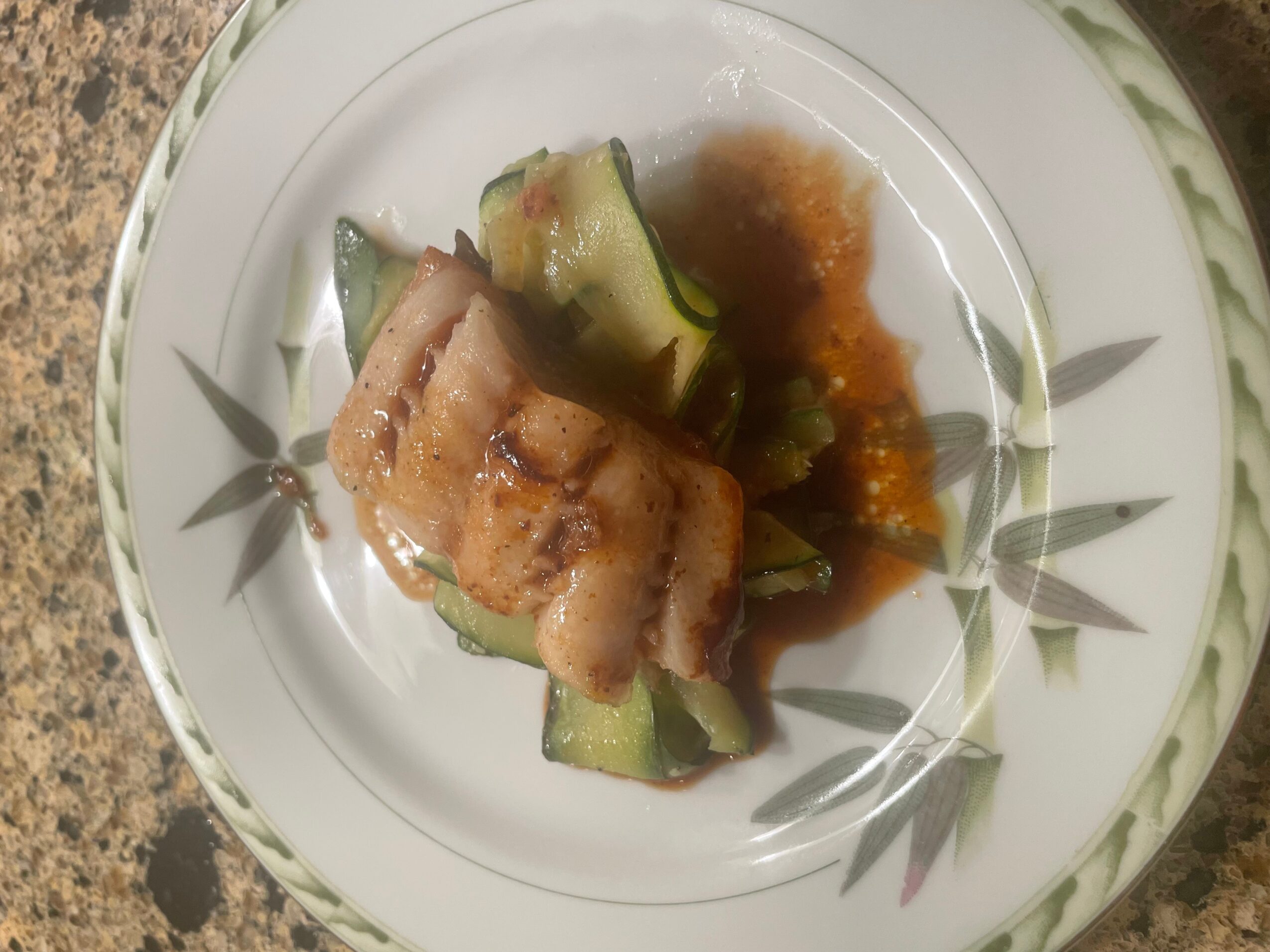 Sliced cucumber with a piece of cooked fish and sauce on a decorative plate.