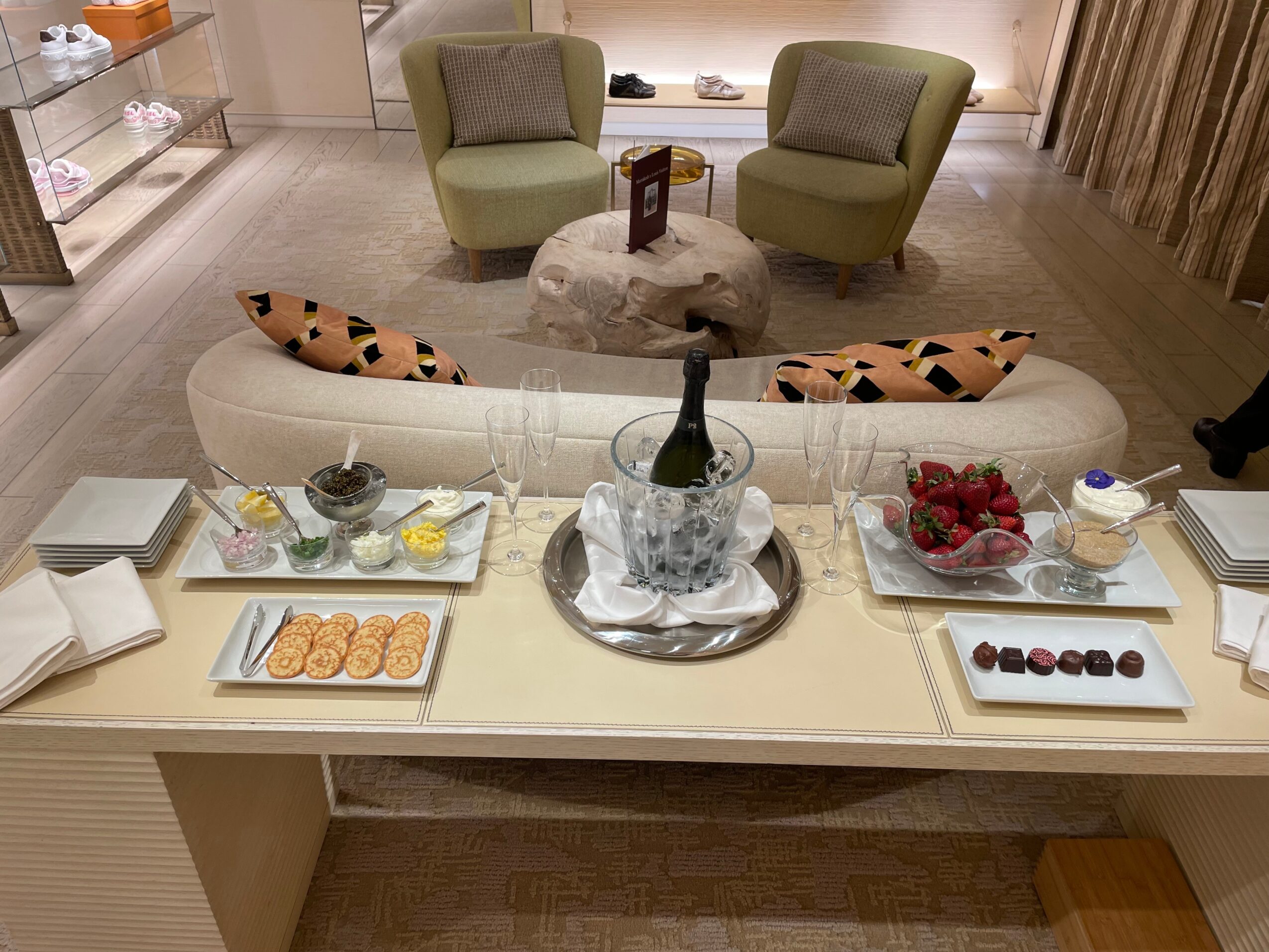Living room with two green armchairs, a white sofa with patterned pillows, and a table with snacks and decorations.