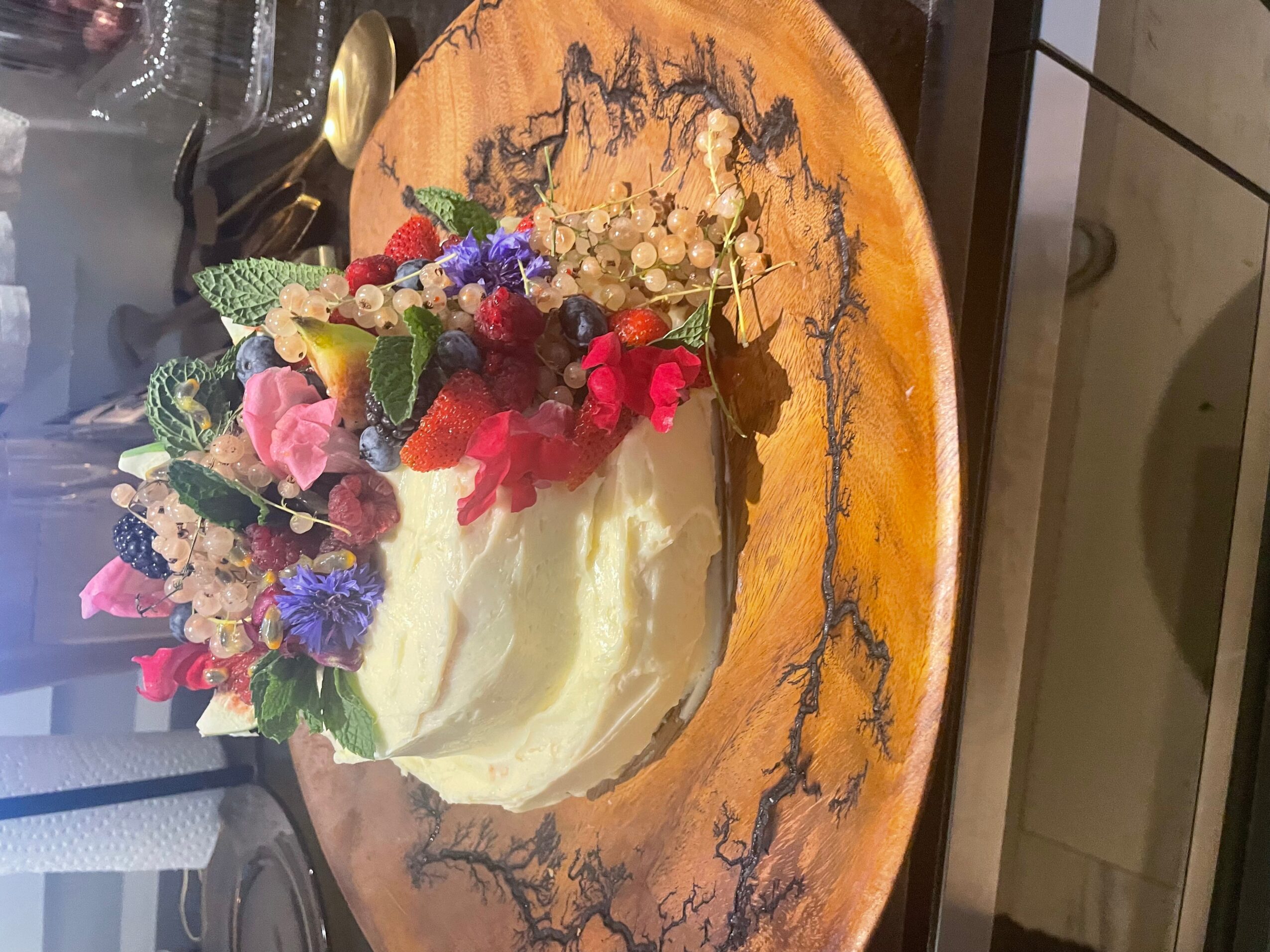 Cake decorated with colorful flowers and greenery on a wooden board.