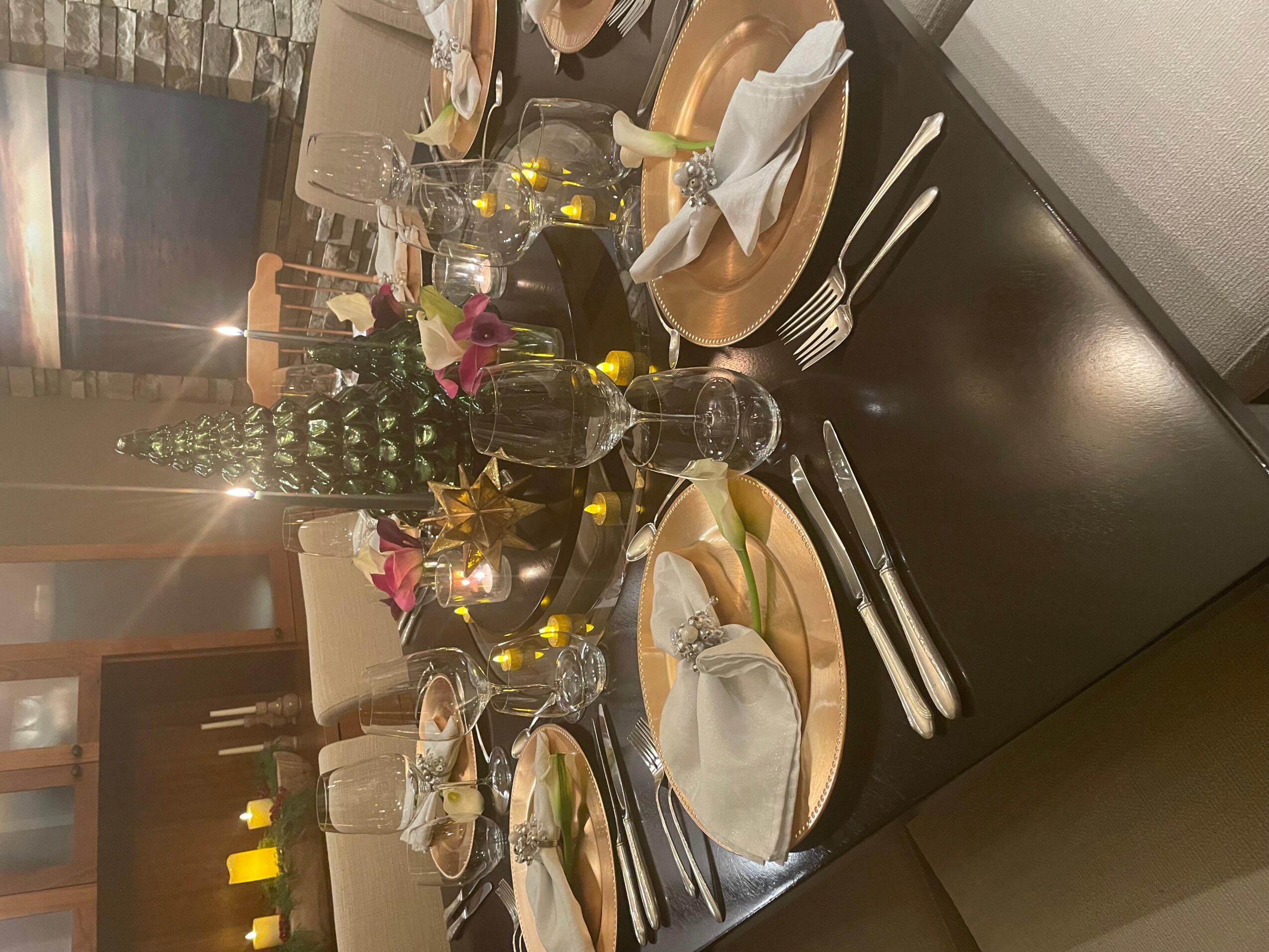 Table set with plates, glasses, cutlery, and a centerpiece with flowers and candles, in a dining room.