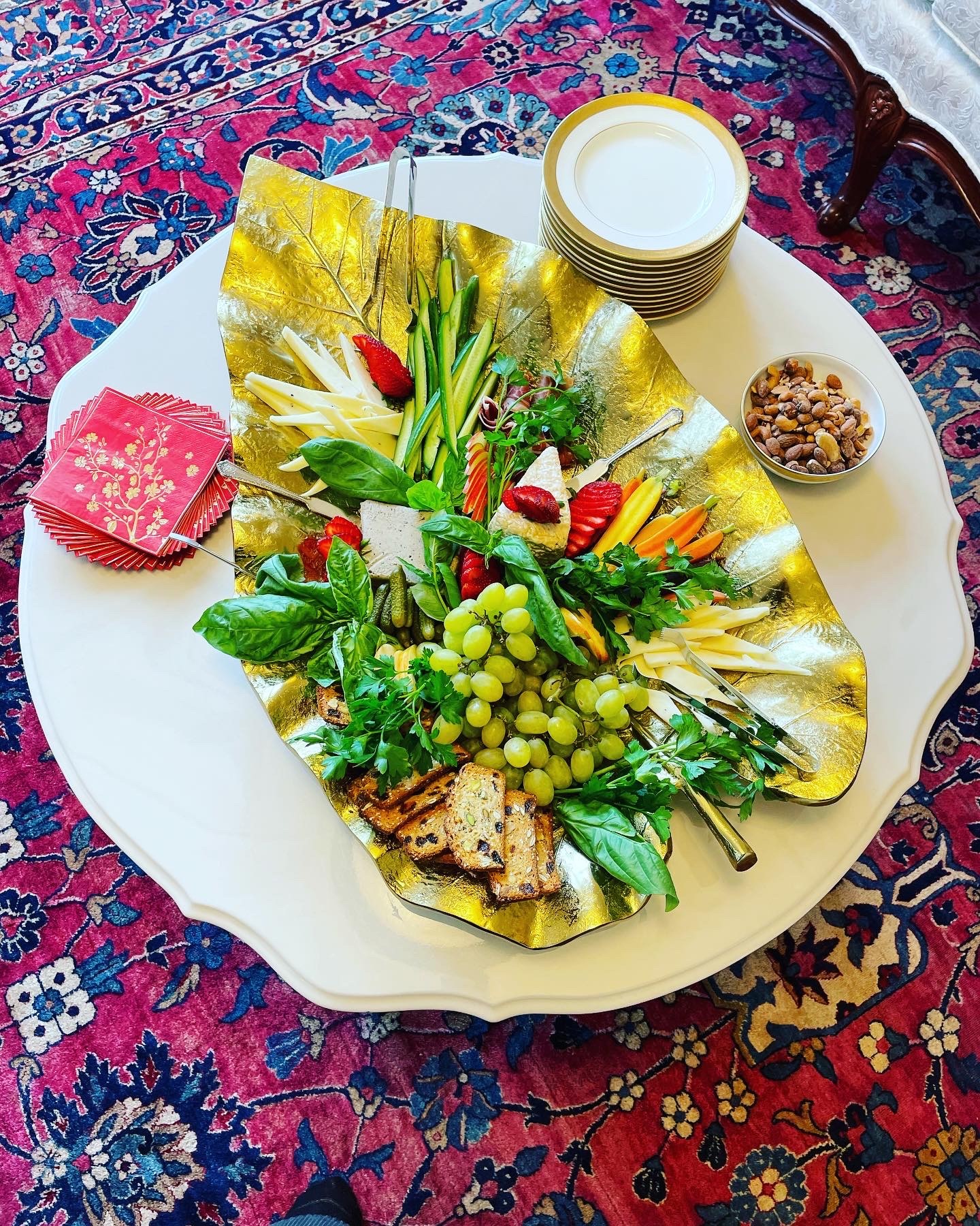 A plate with a salad, bread, a small bowl of nuts, a cup of yogurt, and a pink napkin on a patterned rug.