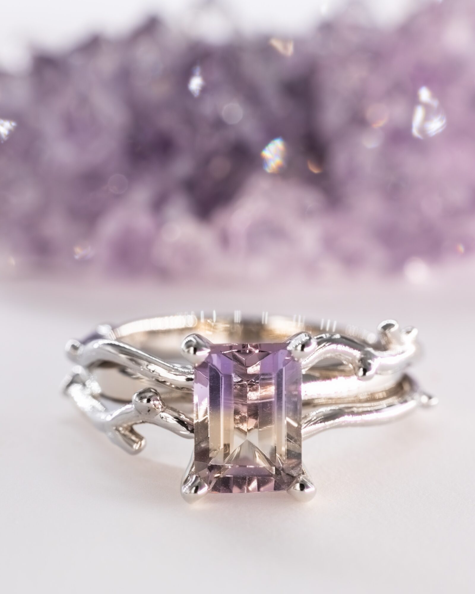 Silver ring with a rectangular purple gemstone, set against a blurred purple background.