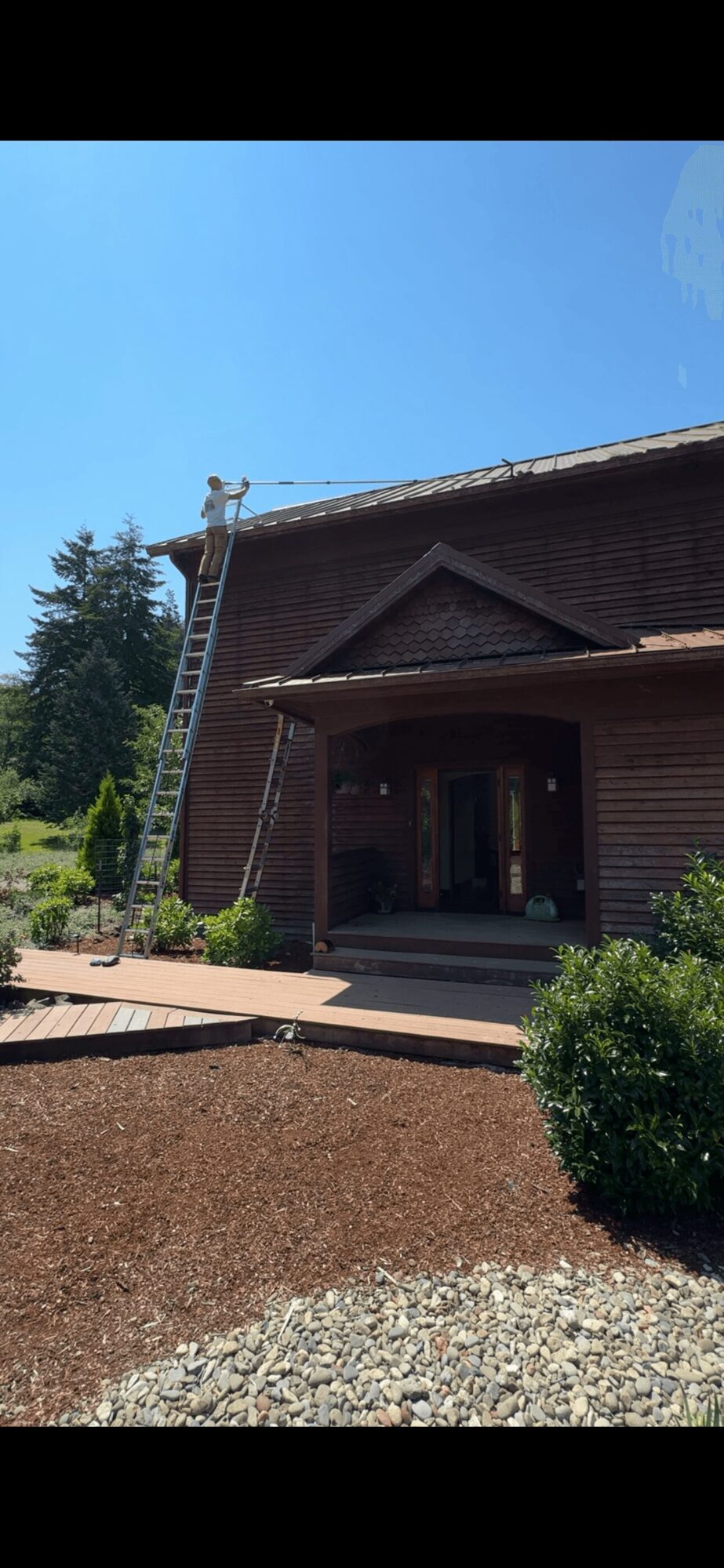 A brick building with a porch, ladder leaning against the wall, and a clear blue sky above.