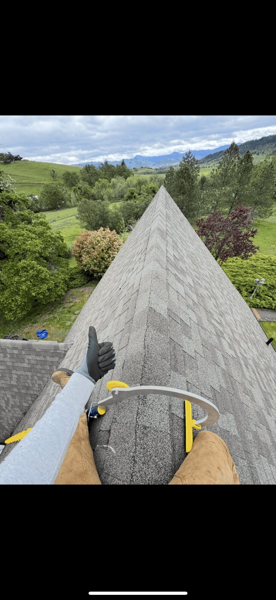 Person wearing gloves on a ladder, working on a roof with a scenic landscape in the background.