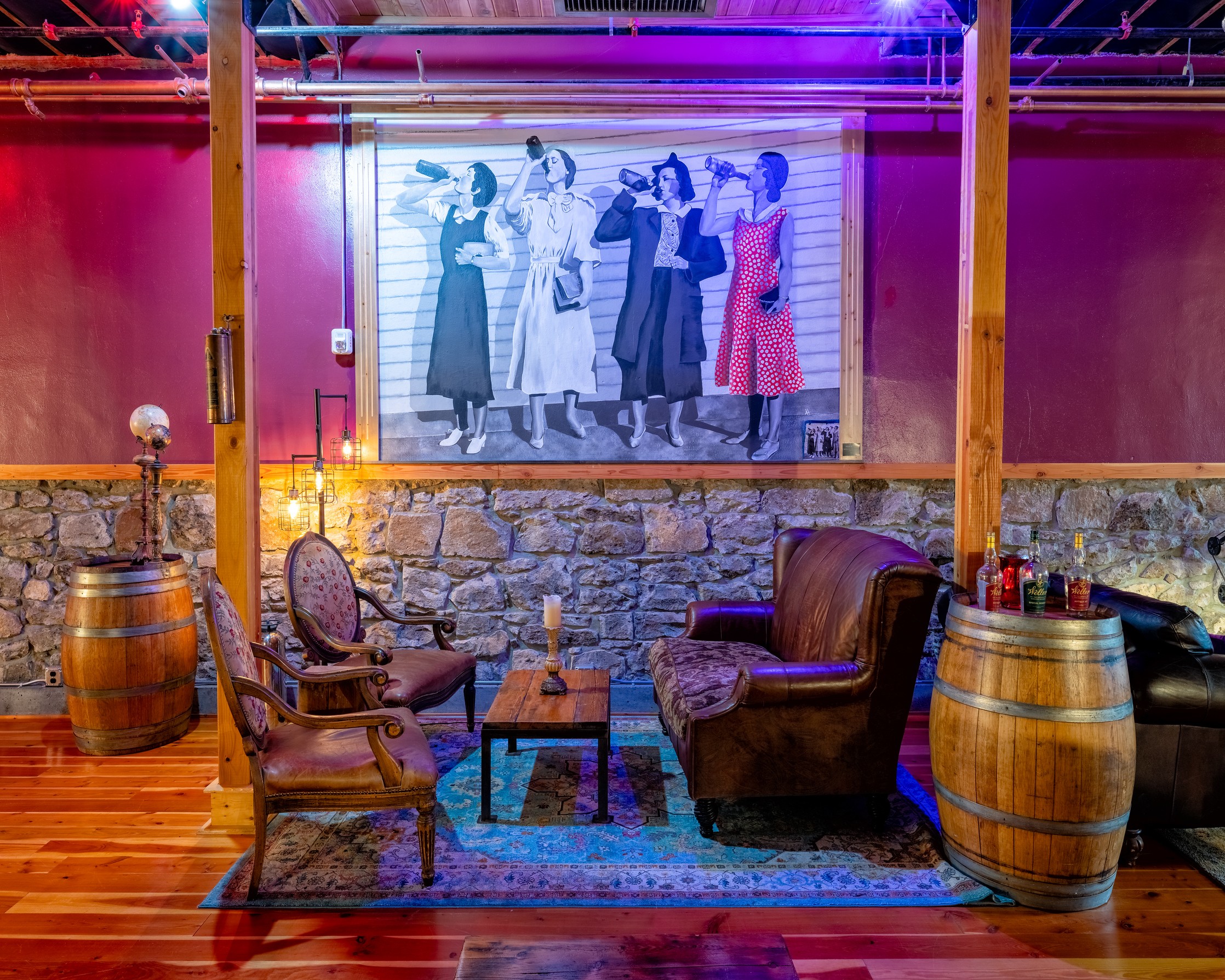 Interior of a cozy room with vintage furniture, a stone wall, and a large mural of women in vintage clothing.