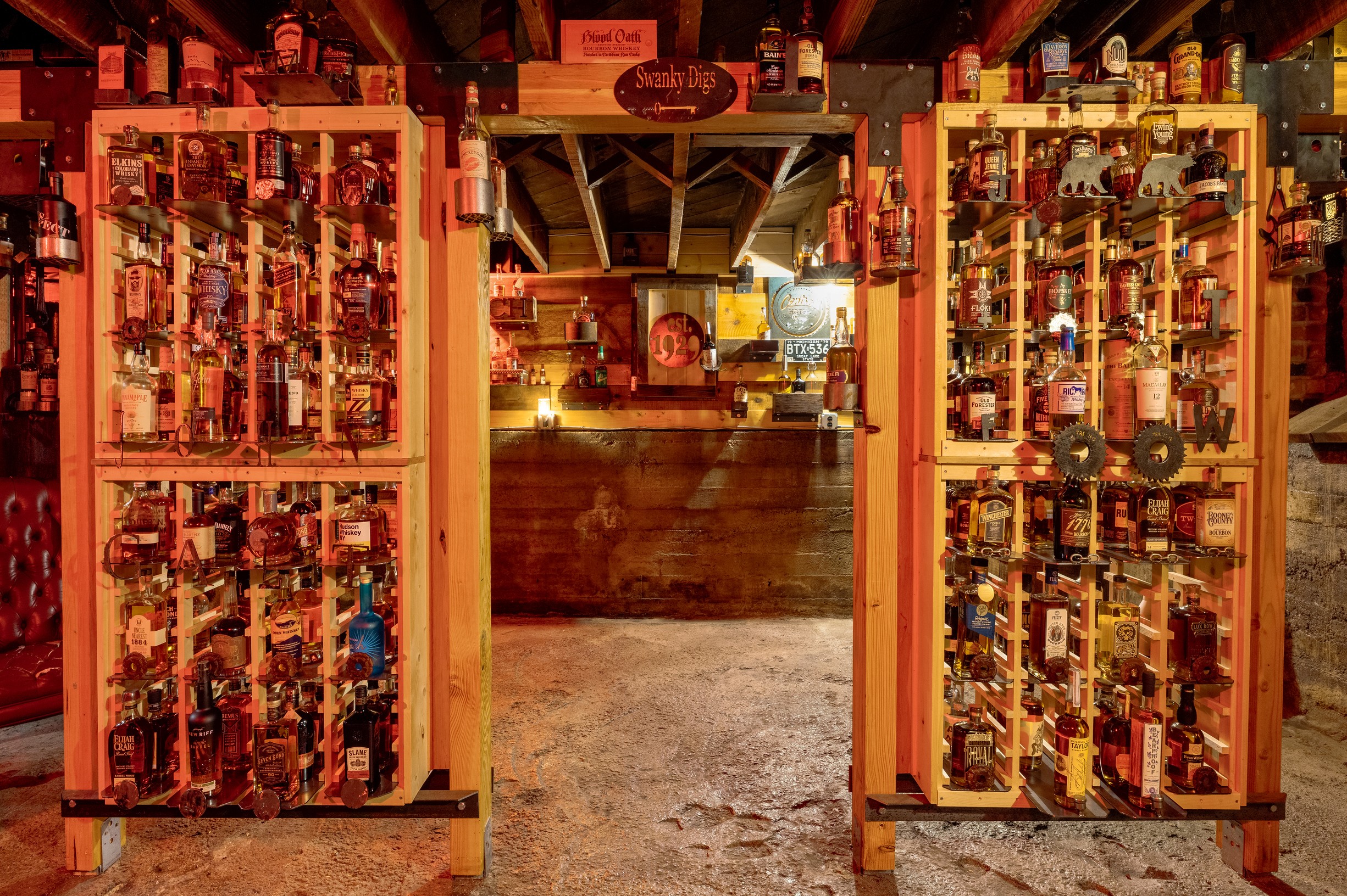 View through open wooden cabinets filled with bottles, leading to a bar area with a counter and shelves behind it.