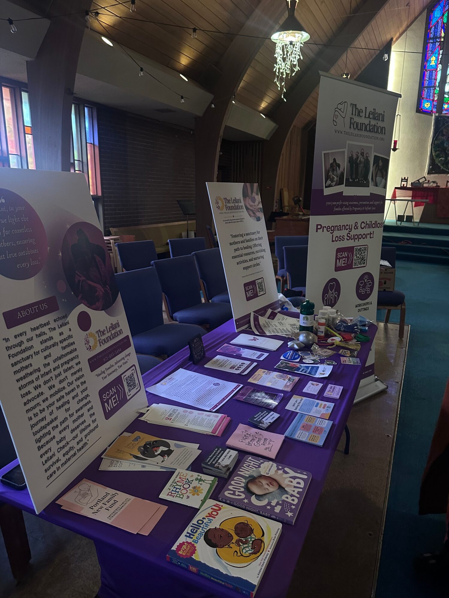 Display table with informational posters, pamphlets, and colorful materials in a room with windows and curtains.
