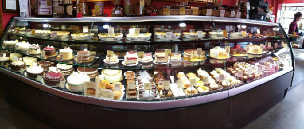 Display case filled with various cakes and desserts in a bakery or cafe setting.