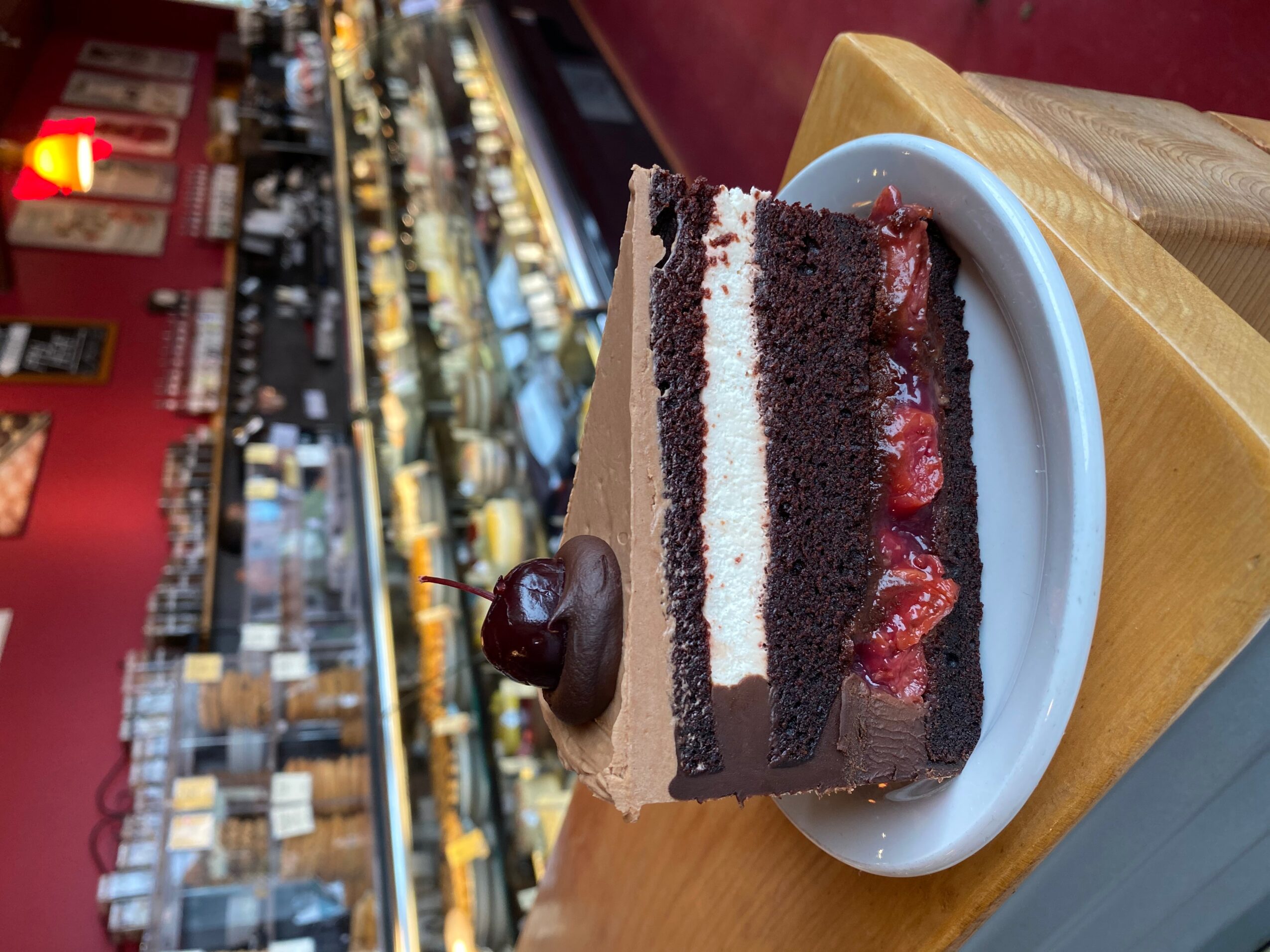Slice of chocolate cake with strawberries and cream on a white plate, on a wooden table in a bakery.