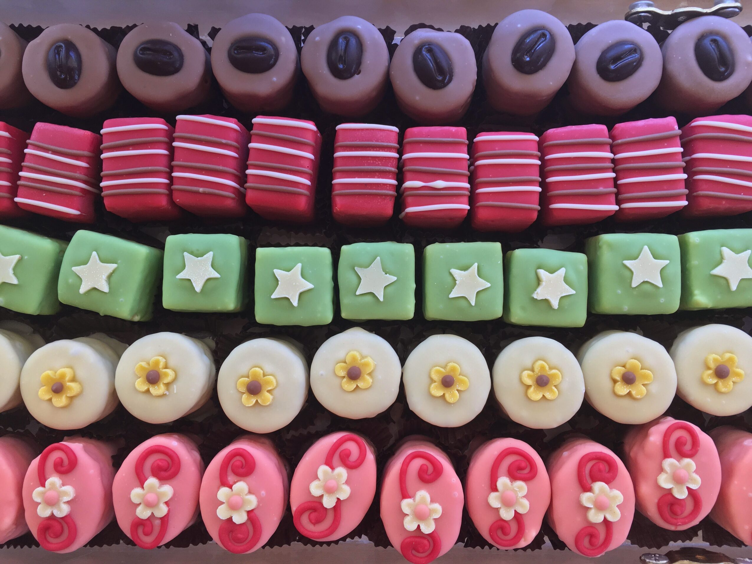 Close-up of colorful candies arranged in rows with various shapes and patterns, including eyes, stripes, stars, flowers, and hearts.