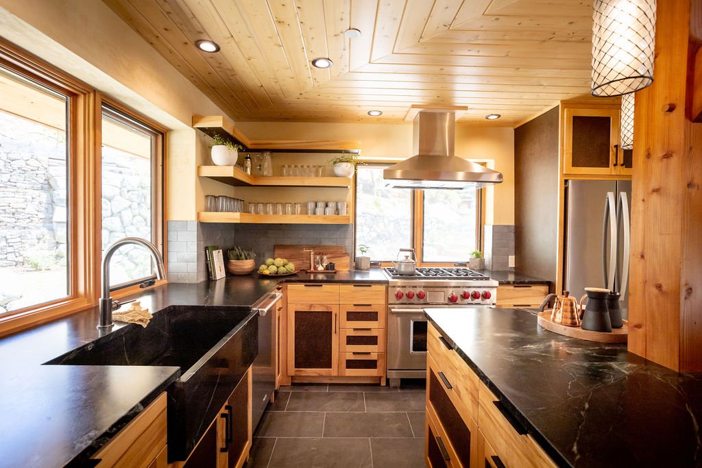 Kitchen with wooden cabinets, black countertops, stainless steel appliances, and large windows, illuminated by natural light.
