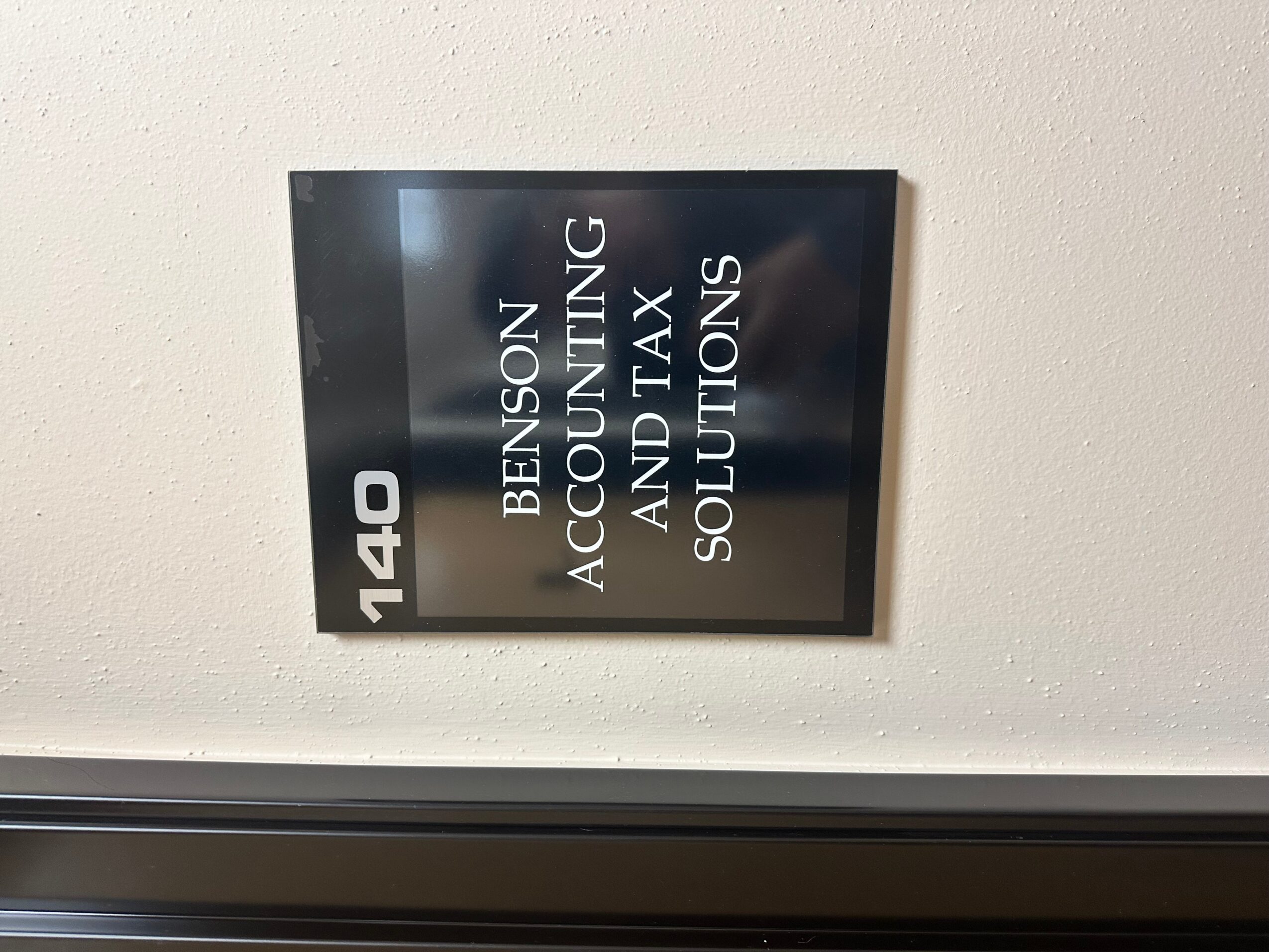 Black sign with white text displaying office number 140 and services related to accounting, tax, and solutions.
