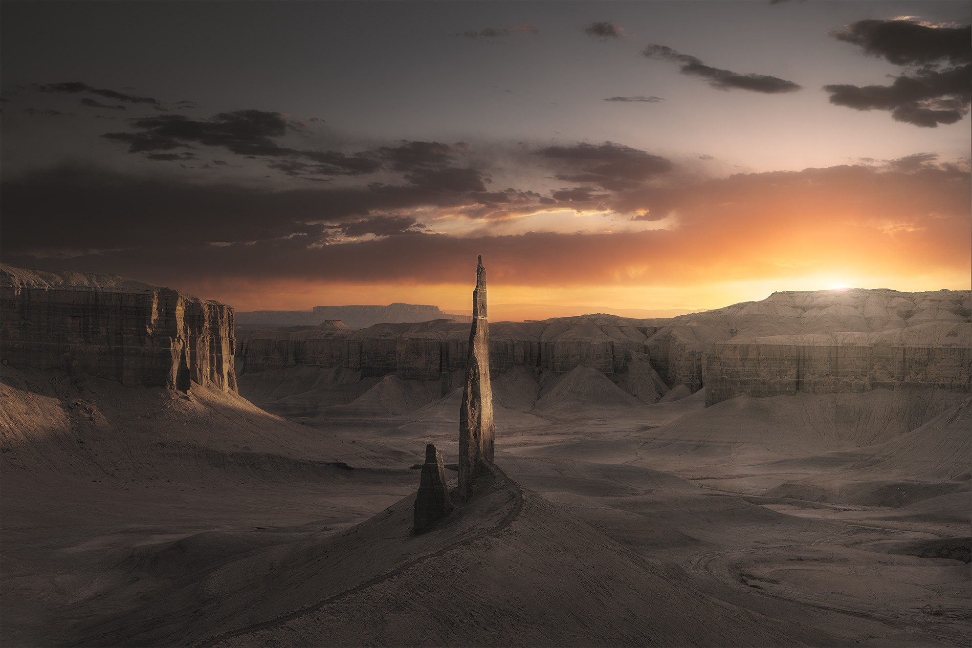Desert landscape with tall rock formations and a person walking along a path at sunset, dark clouds overhead.