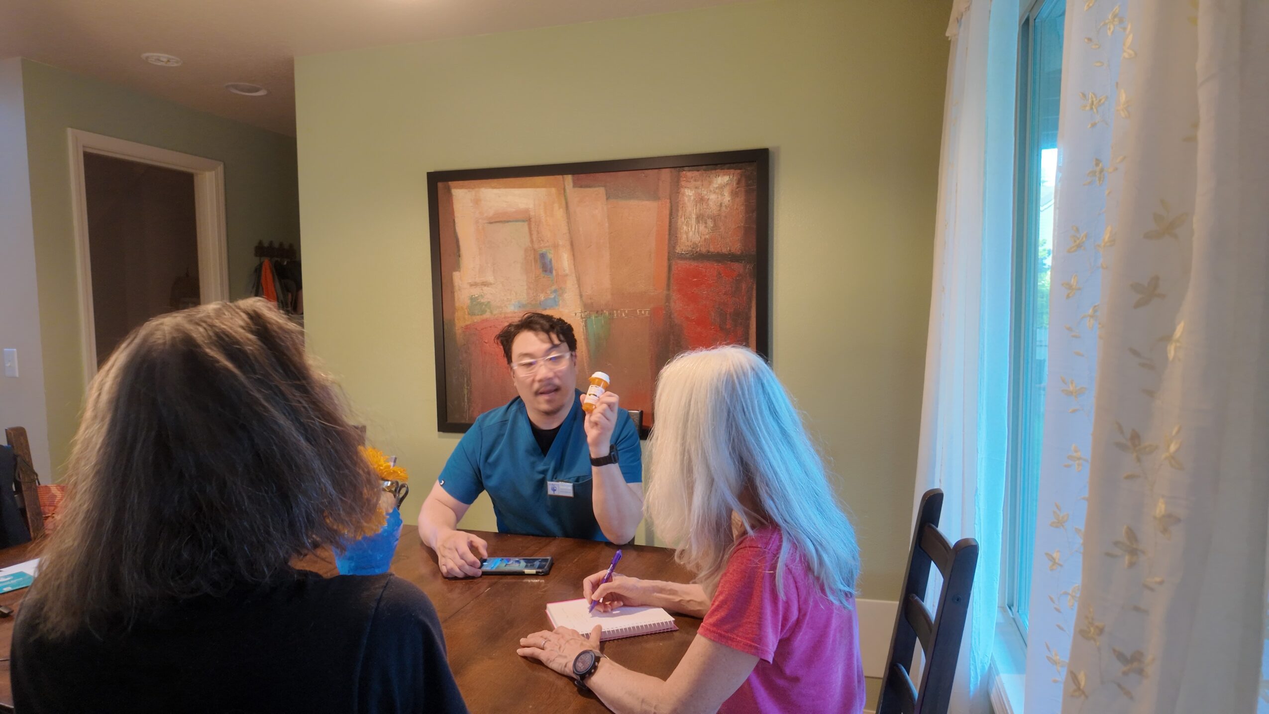 Three people sitting at a table in a room with a green wall and a large painting, engaged in conversation.
