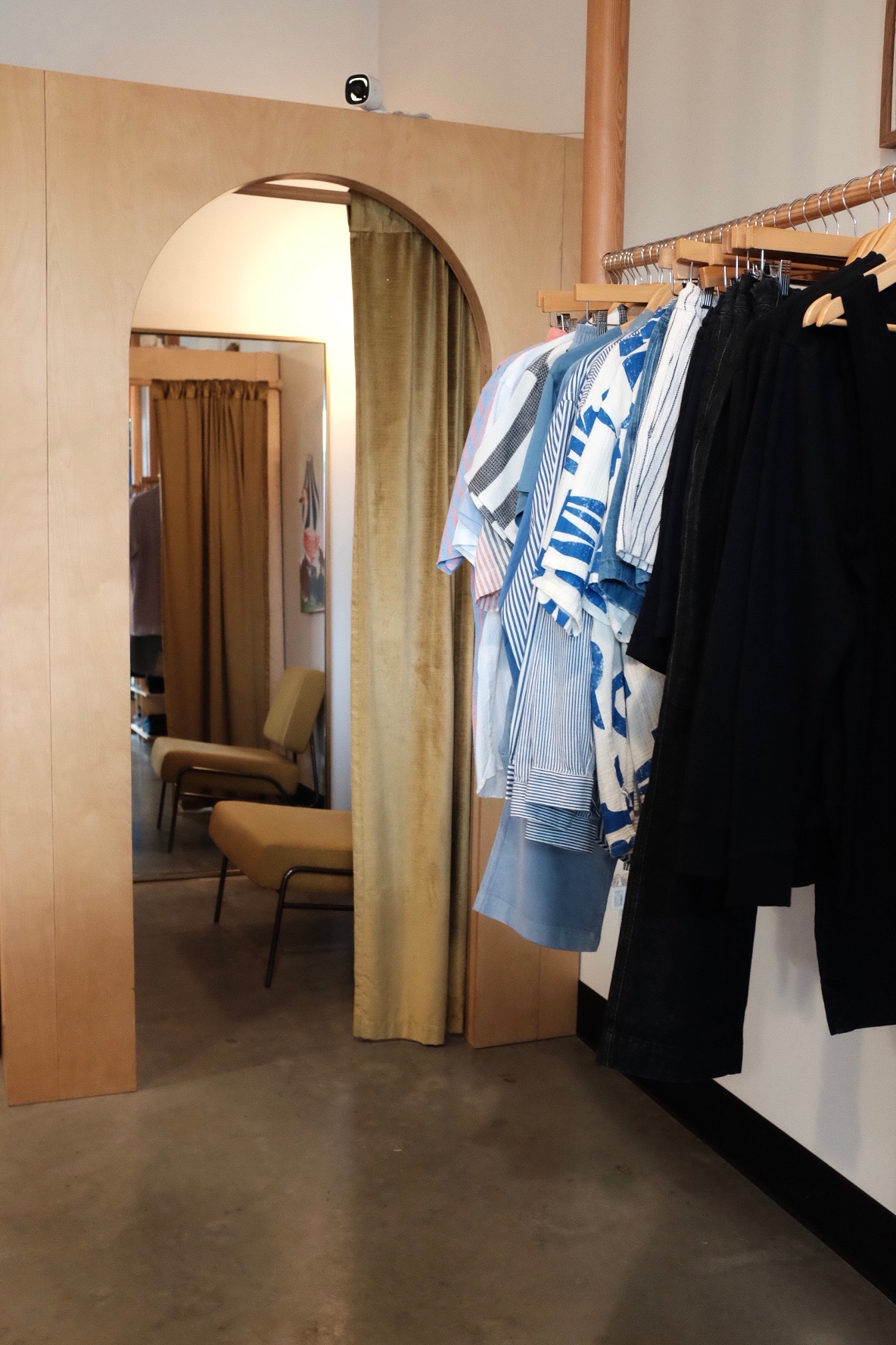 Clothing rack with blue and white garments in a fitting room area, mirror and chair visible in the background.