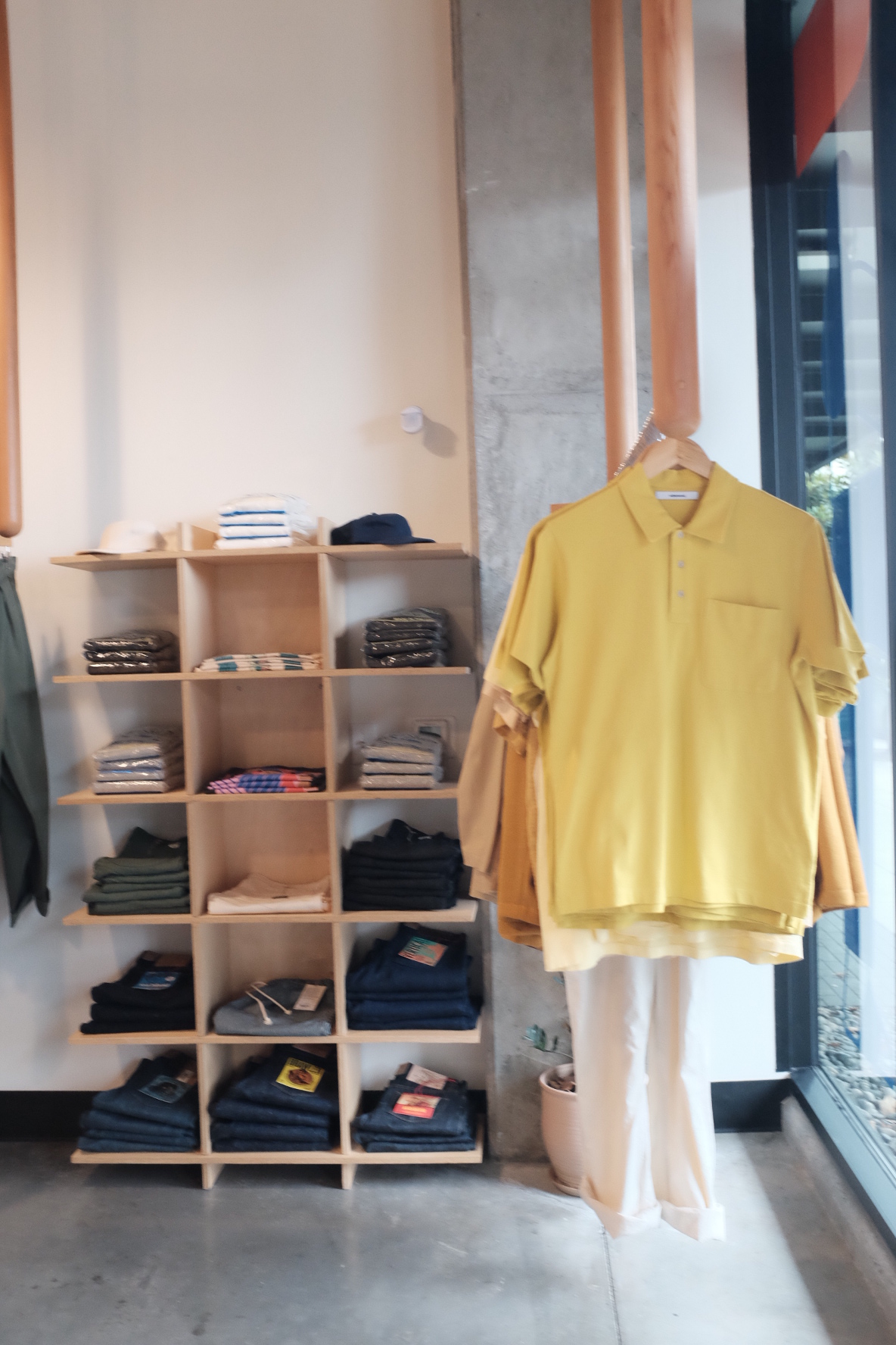 Yellow shirt hanging on a wooden hanger in front of a shoe shelf with various shoes, wall, and floor visible.