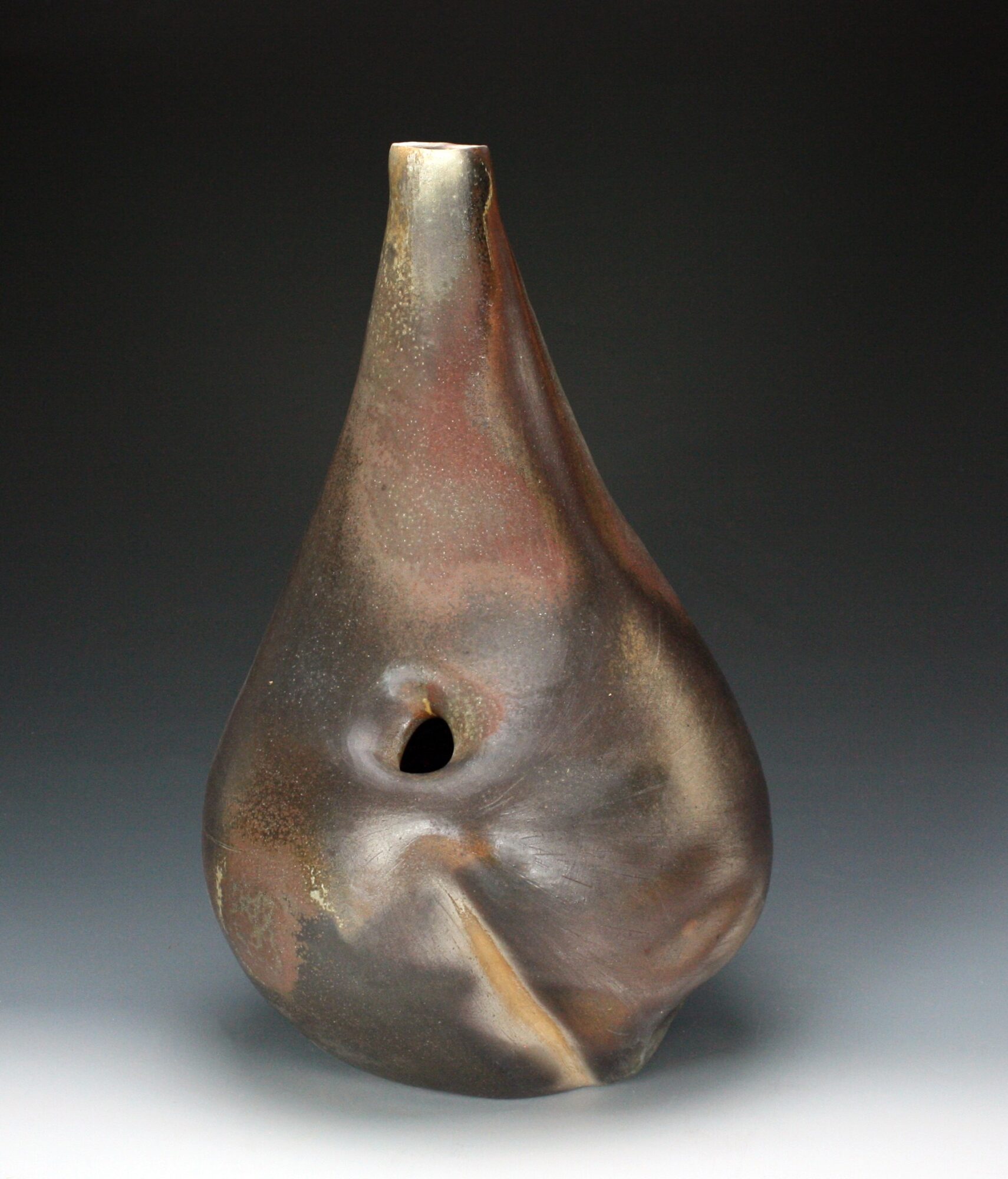 Ceramic vase with a narrow neck and rounded body, featuring a small hole and a textured surface, against a dark background.