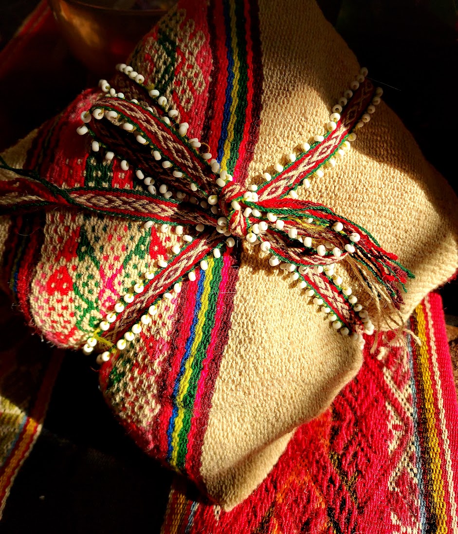 Wrapped gift with colorful woven fabric and a decorative bow, placed on a patterned textile surface.