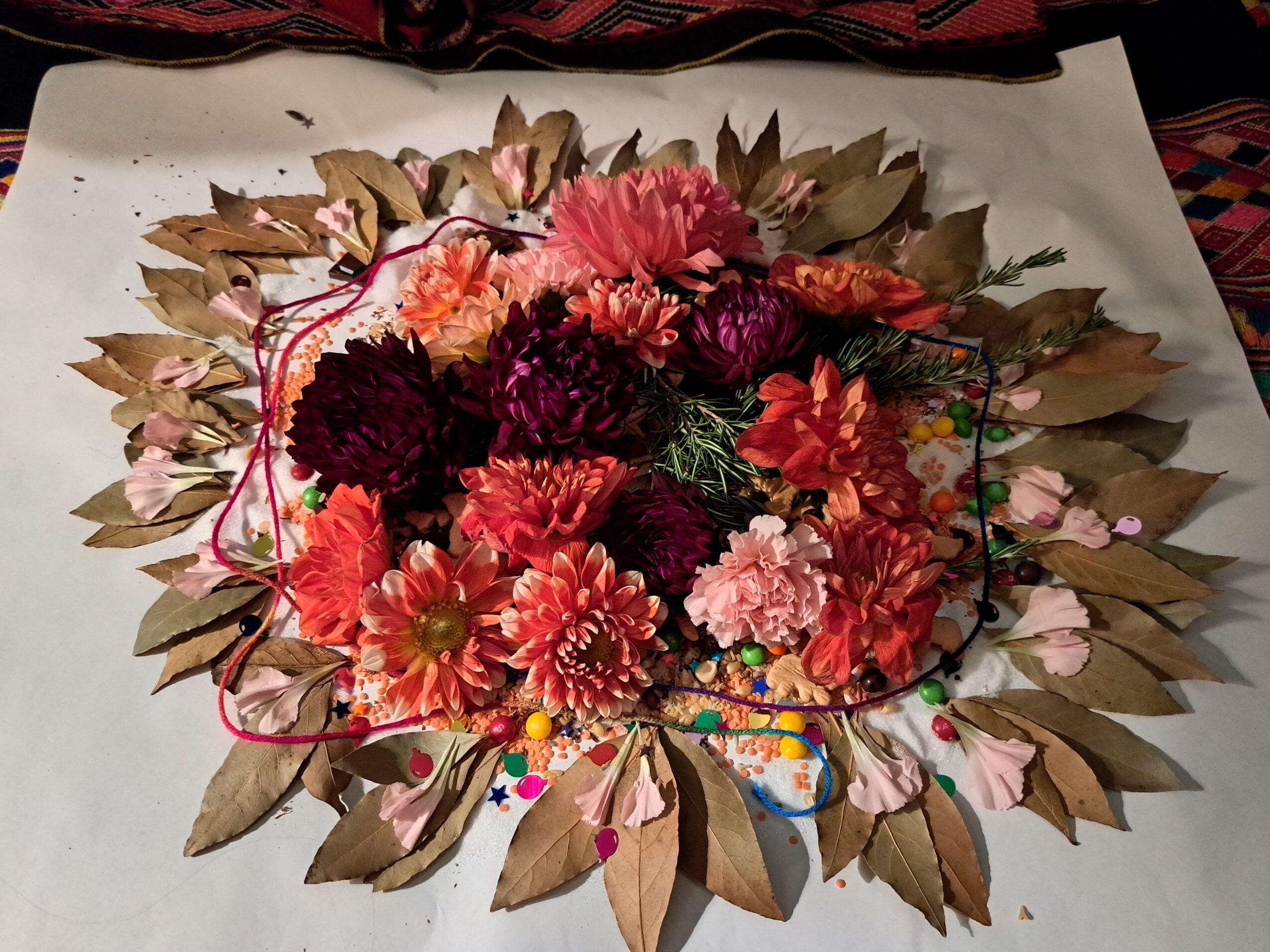 Arrangement of pink, red, and purple flowers with green leaves on white paper, surrounded by a brown leaf border.