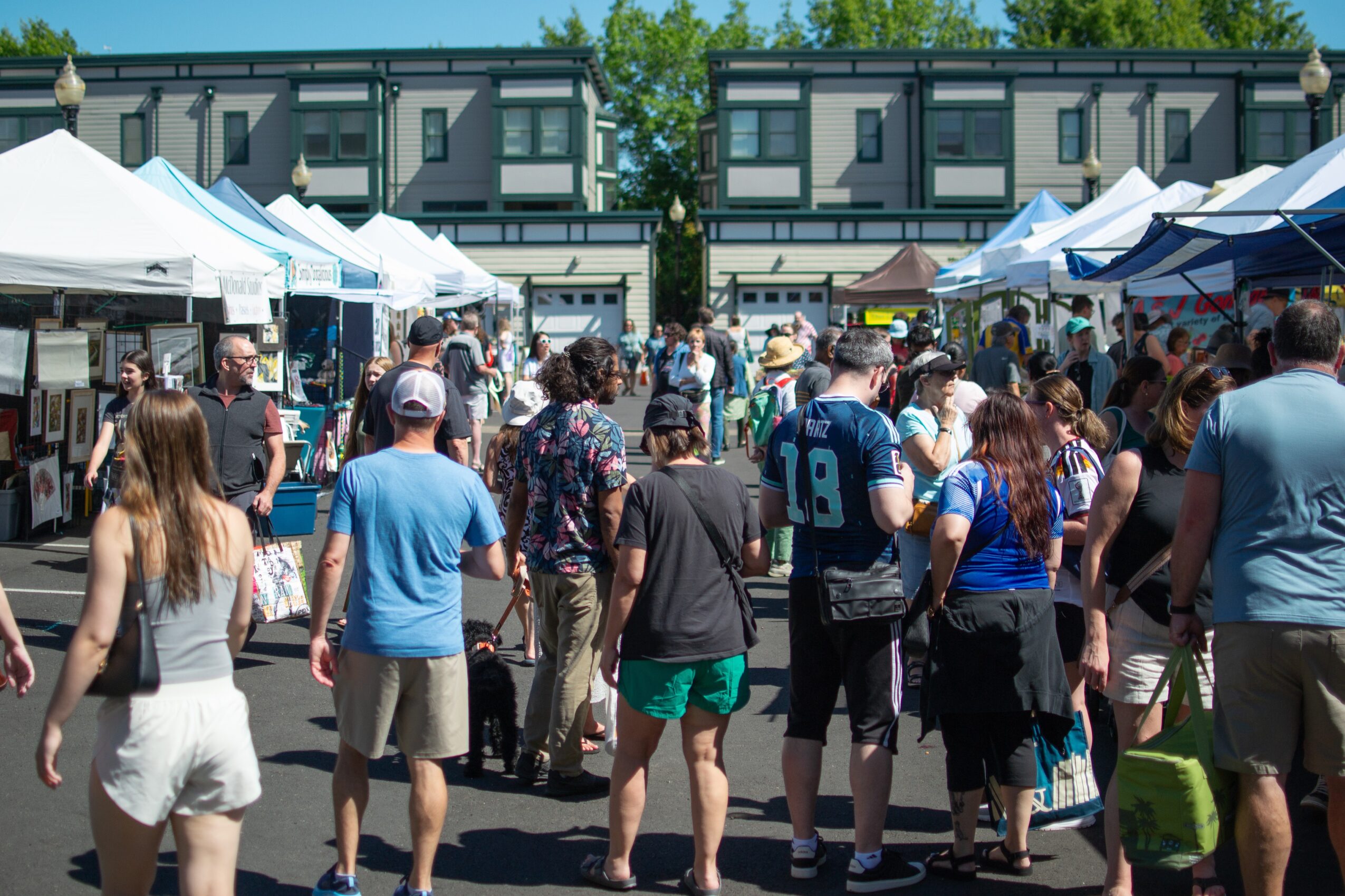 Crowd of people at outdoor market with tents and buildings in background.