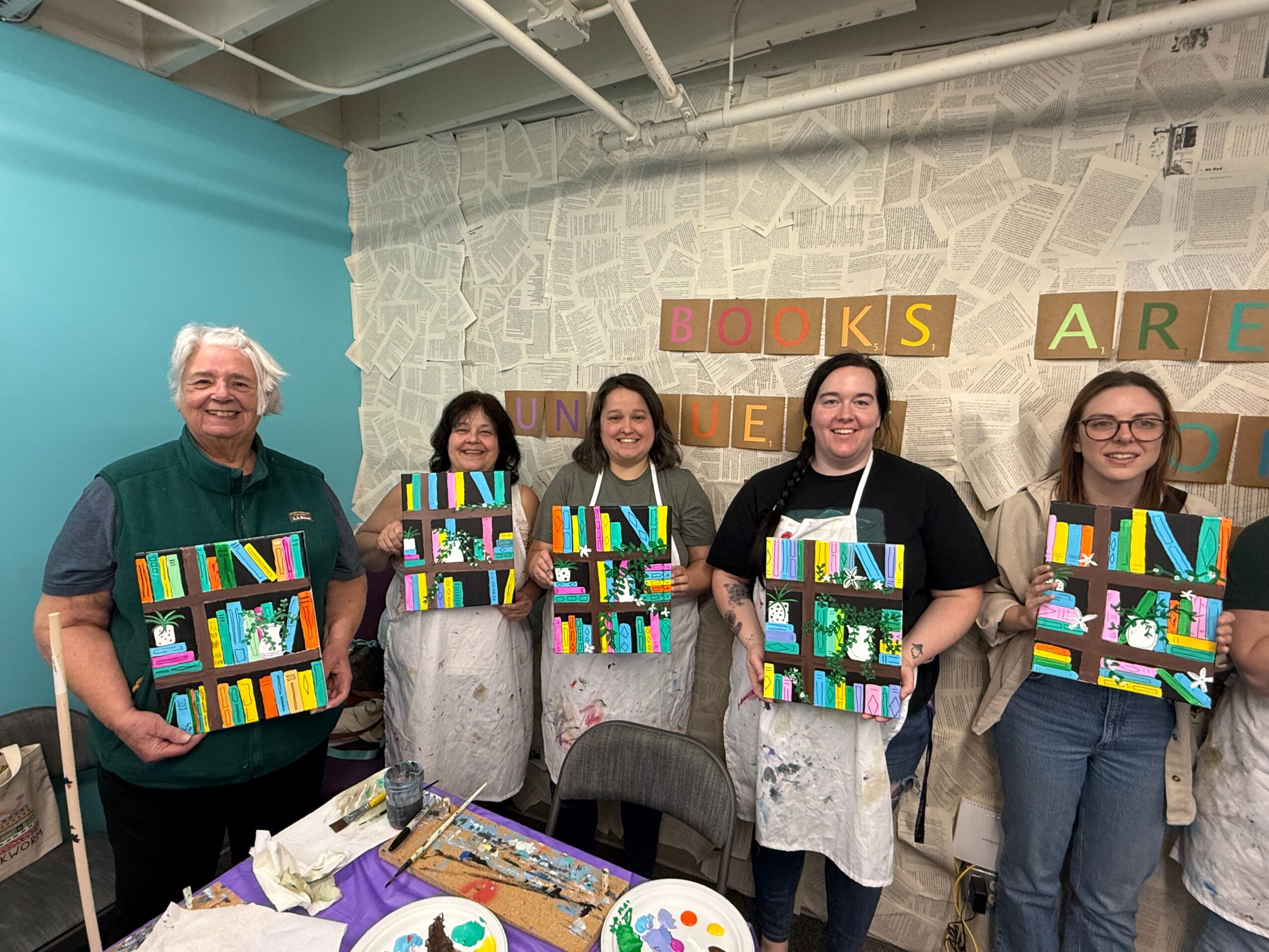 Five people holding colorful books in a room with a wall decorated with blocks spelling words, smiling at the camera.