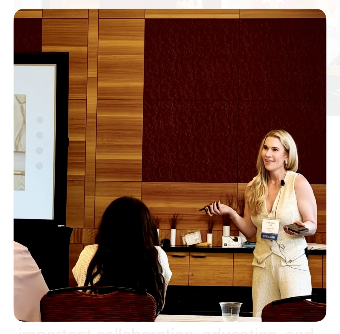 Woman presenting to a group in a conference room with wood-paneled walls.