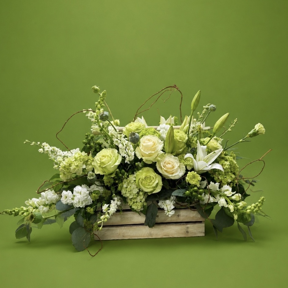White floral arrangement in a wooden box with green background