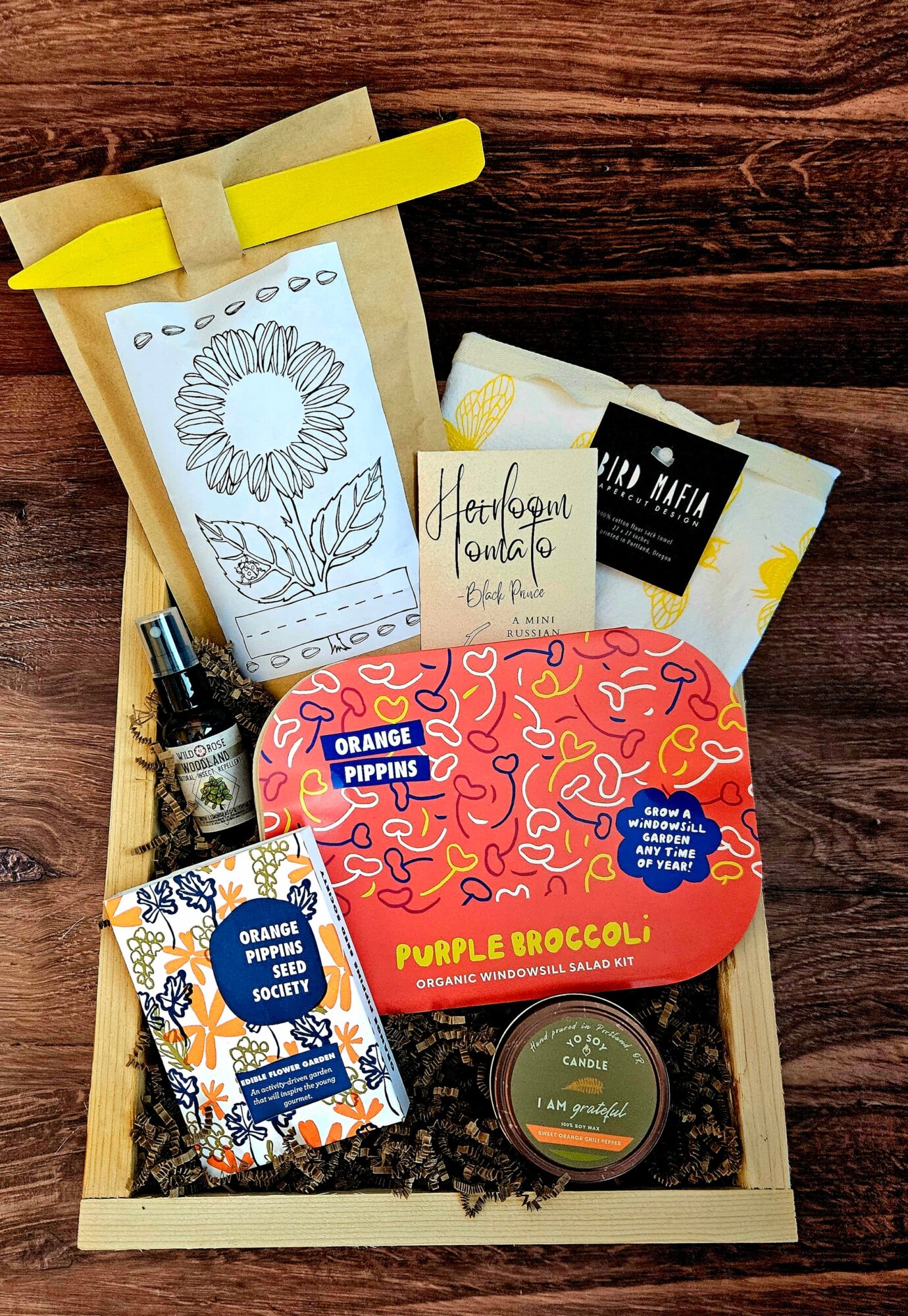 Gift box with coloring book, scented candle, soap, and snacks on a wooden surface.