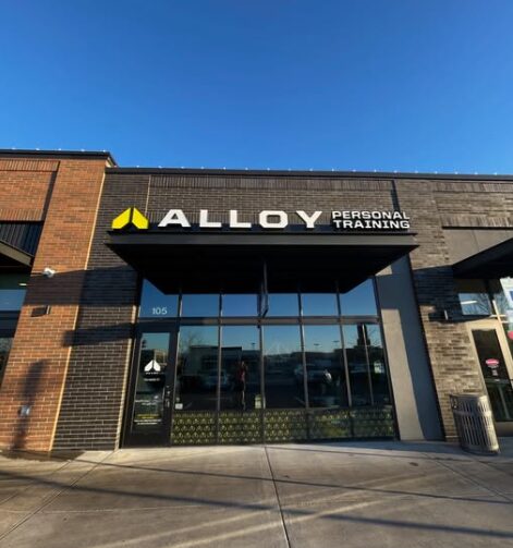 Storefront with sign reading 'ALLOY PERSONAL TRAINING' against a blue sky, glass doors, and brick exterior.
