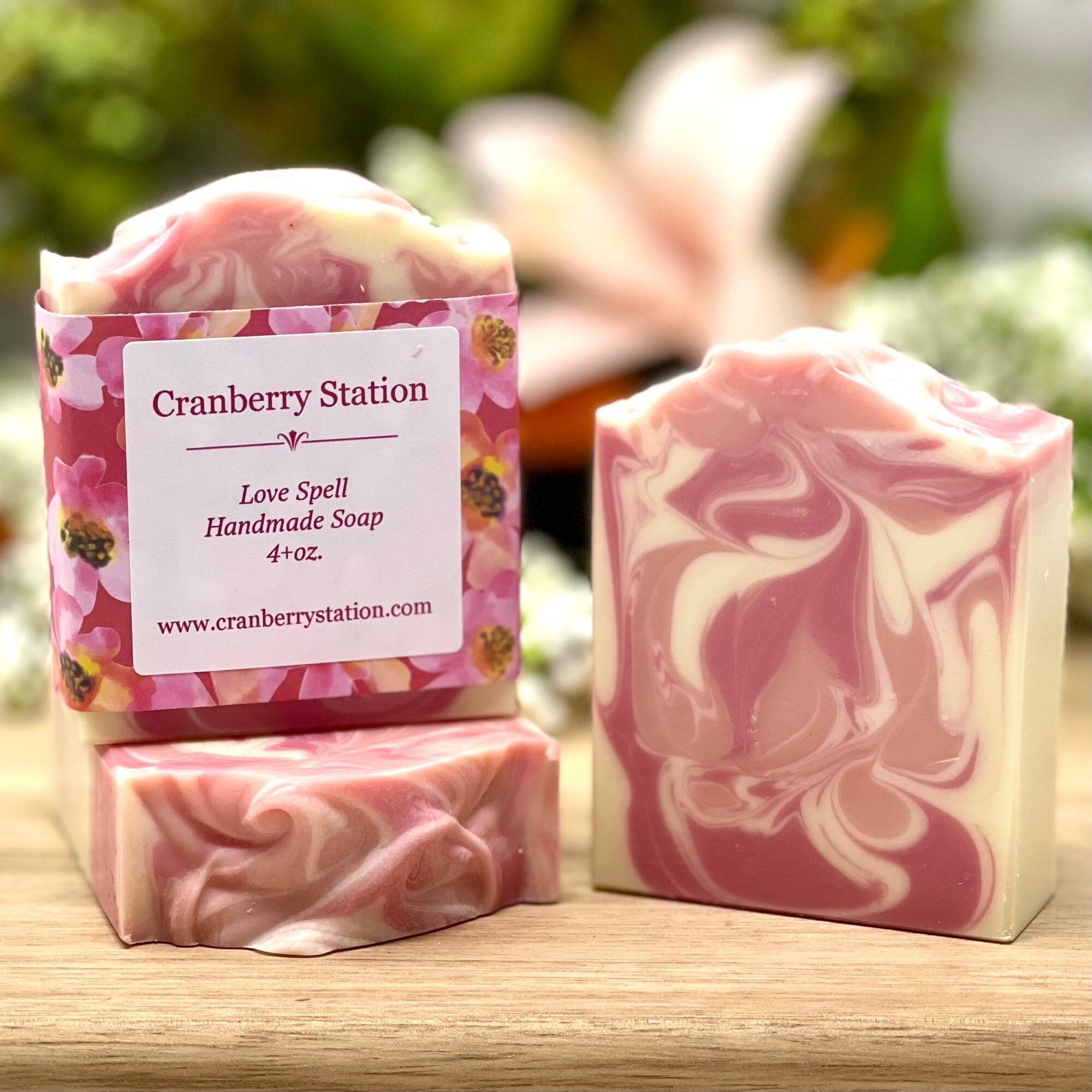 Two handmade soap bars with pink and white marbled patterns, one with a label, on a wooden surface with blurred background.