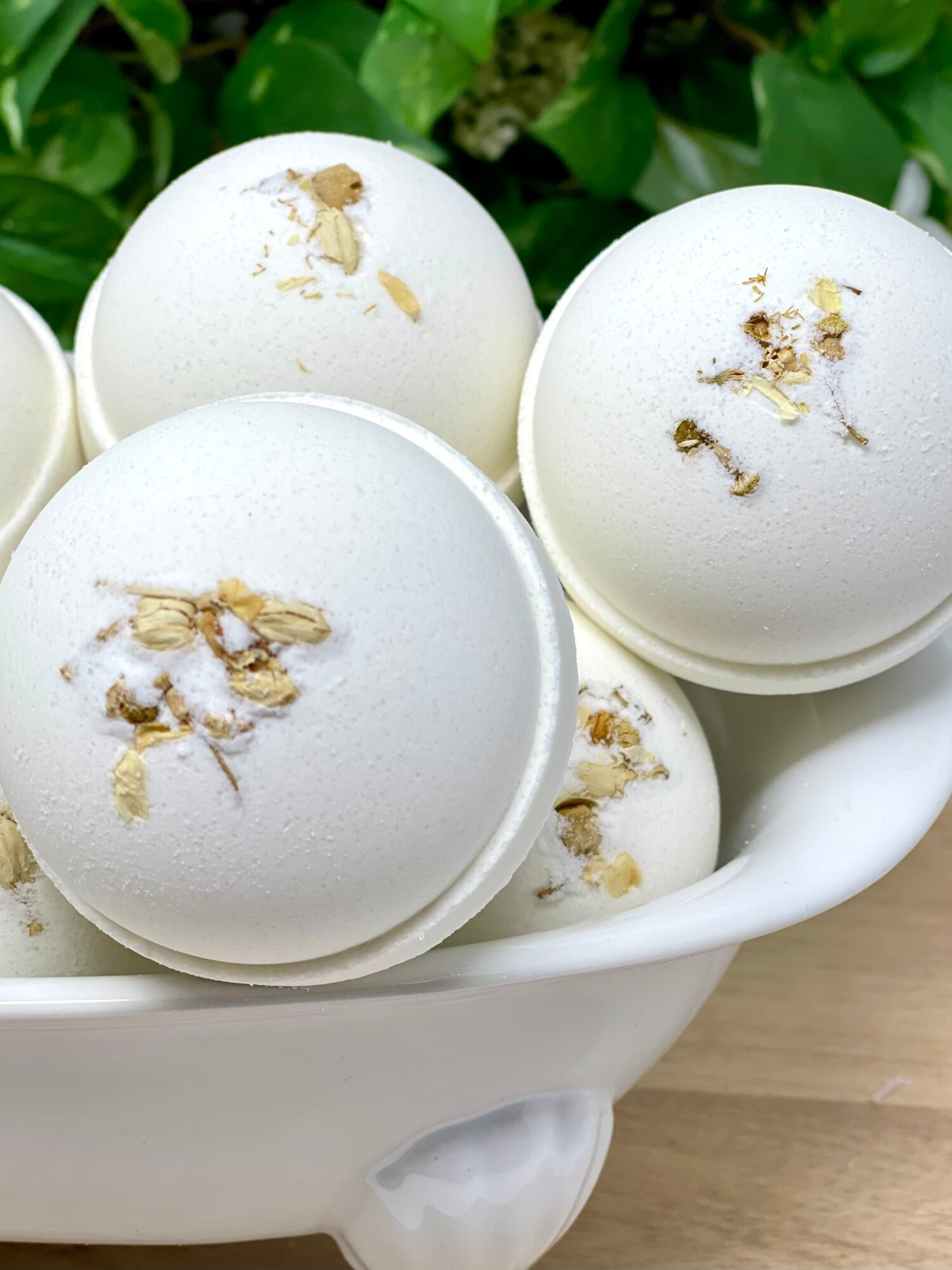 White eggs in a bowl with green leaves in the background, some eggs have brown spots or marks on them.