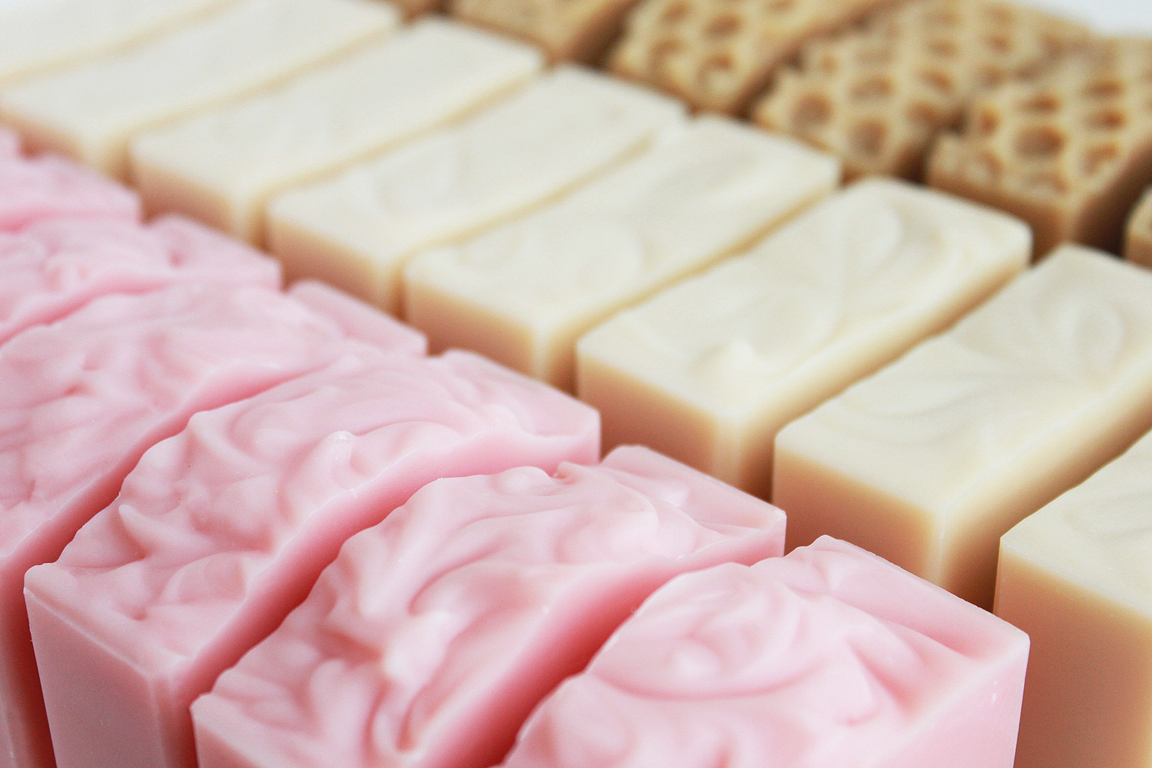 Rows of pink, white, and brown soap bars arranged in a display, with textured and smooth surfaces.