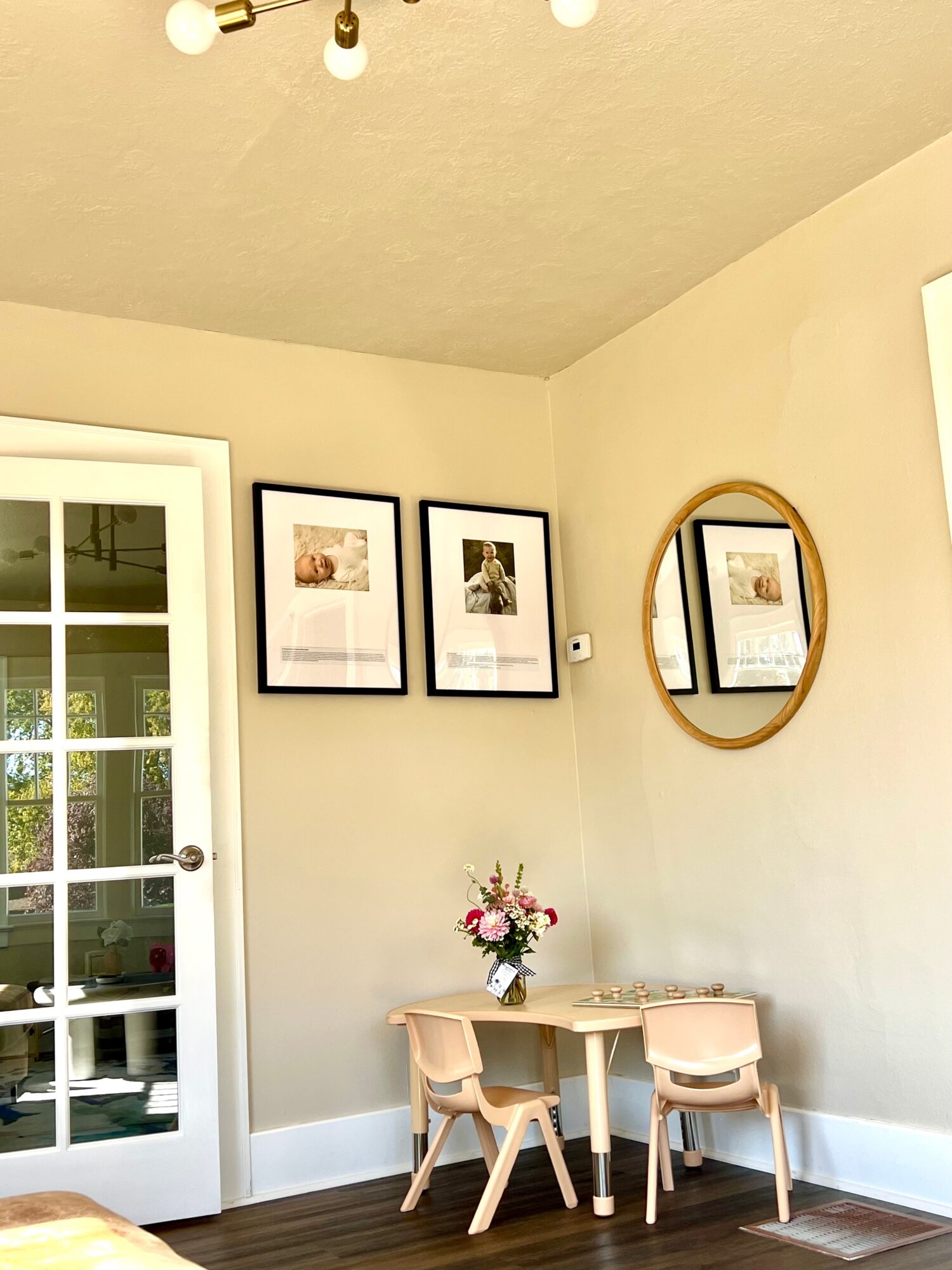 Children's table with three chairs, a vase with flowers, and a round mirror on the wall.