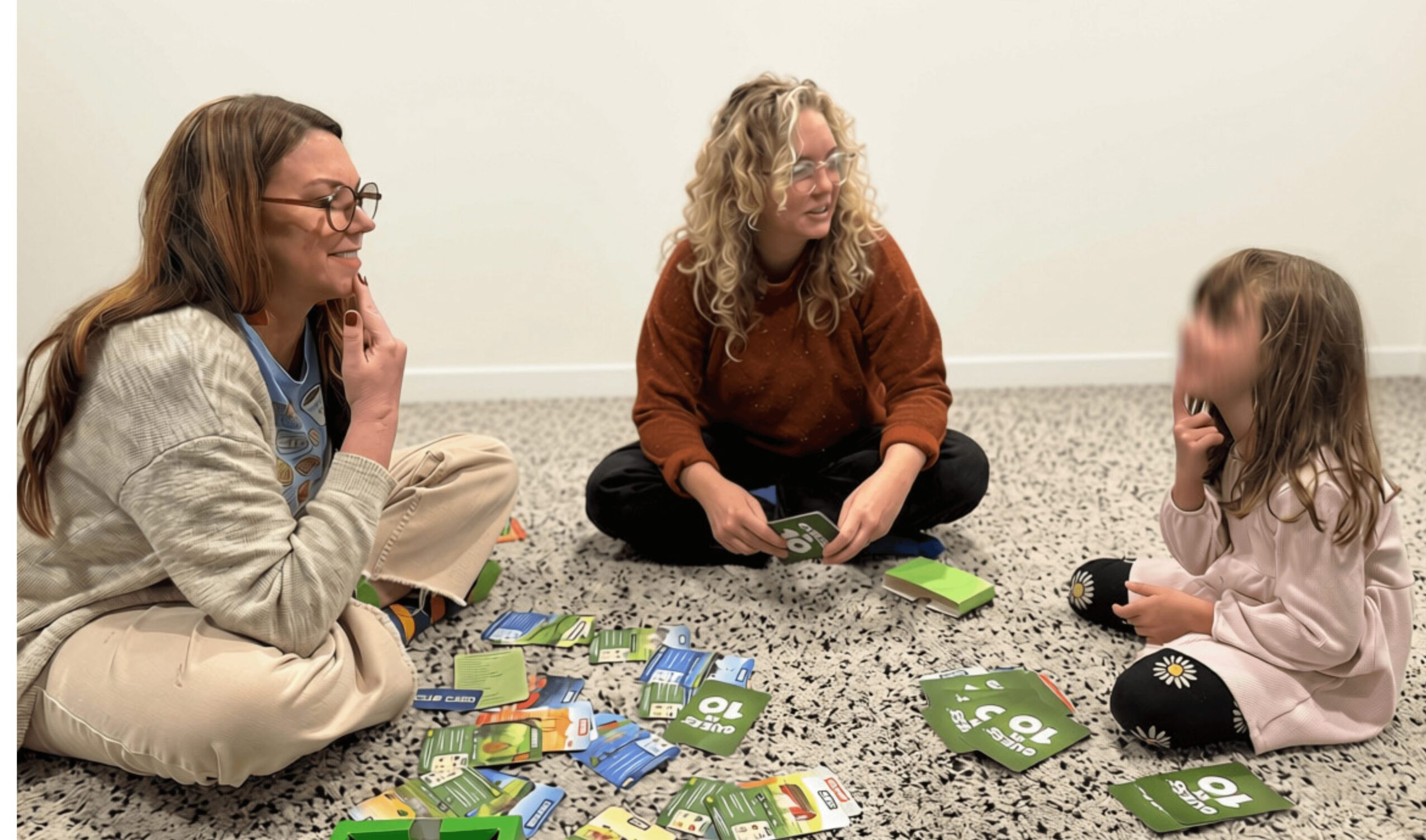 Three people sitting on the floor playing a card game with scattered cards around them.