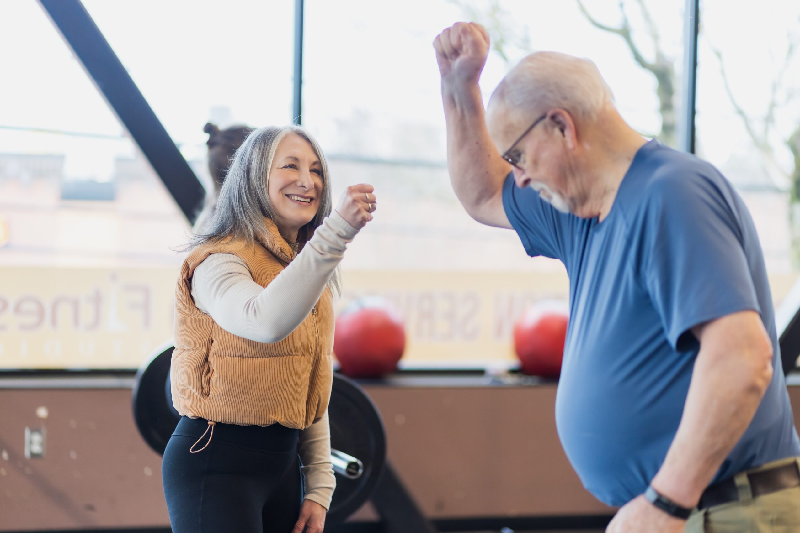 A woman and an older man are celebrating with raised fists in a gym, smiling at each other.