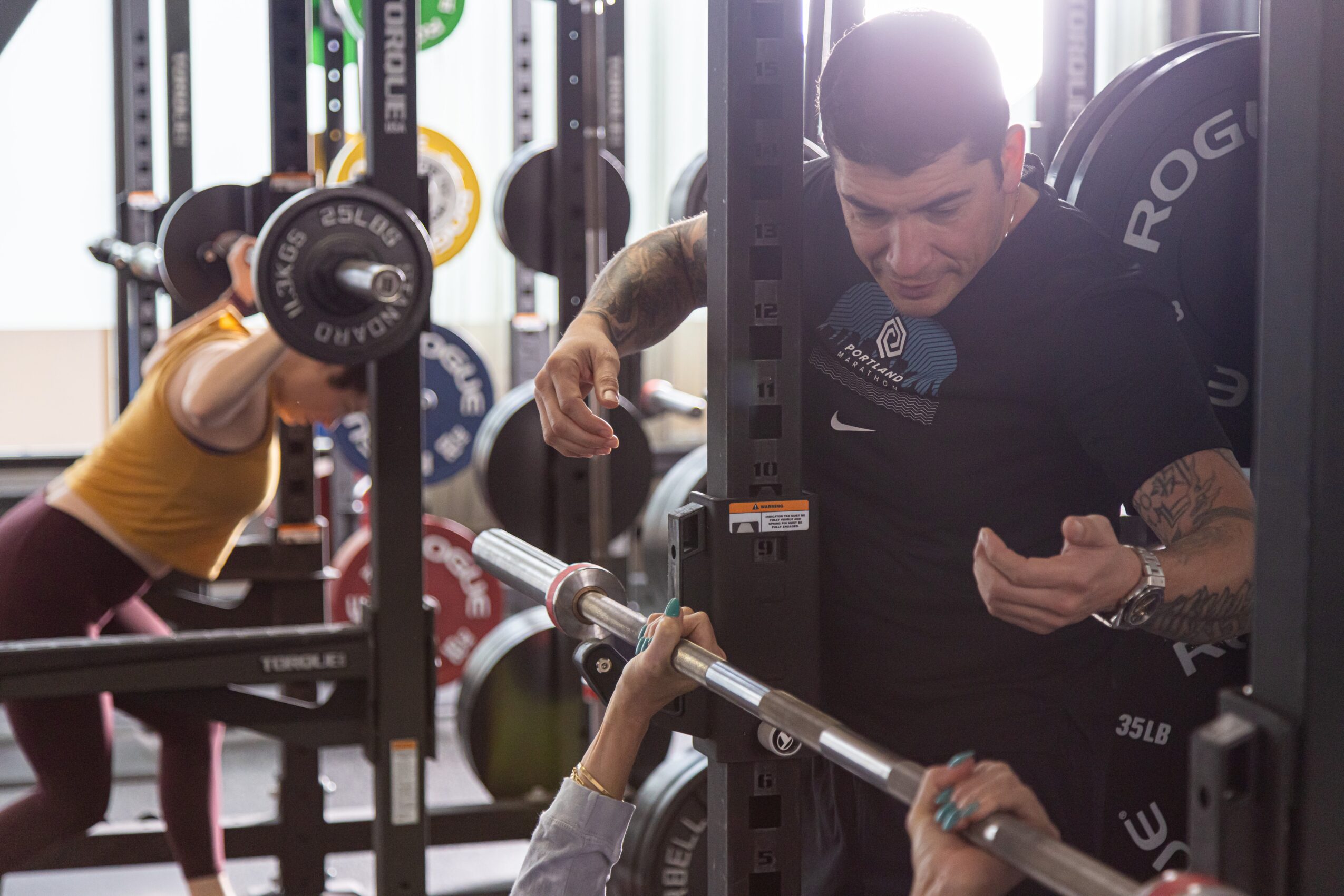 Person lifting weights in a gym with weight plates and equipment visible in the background.