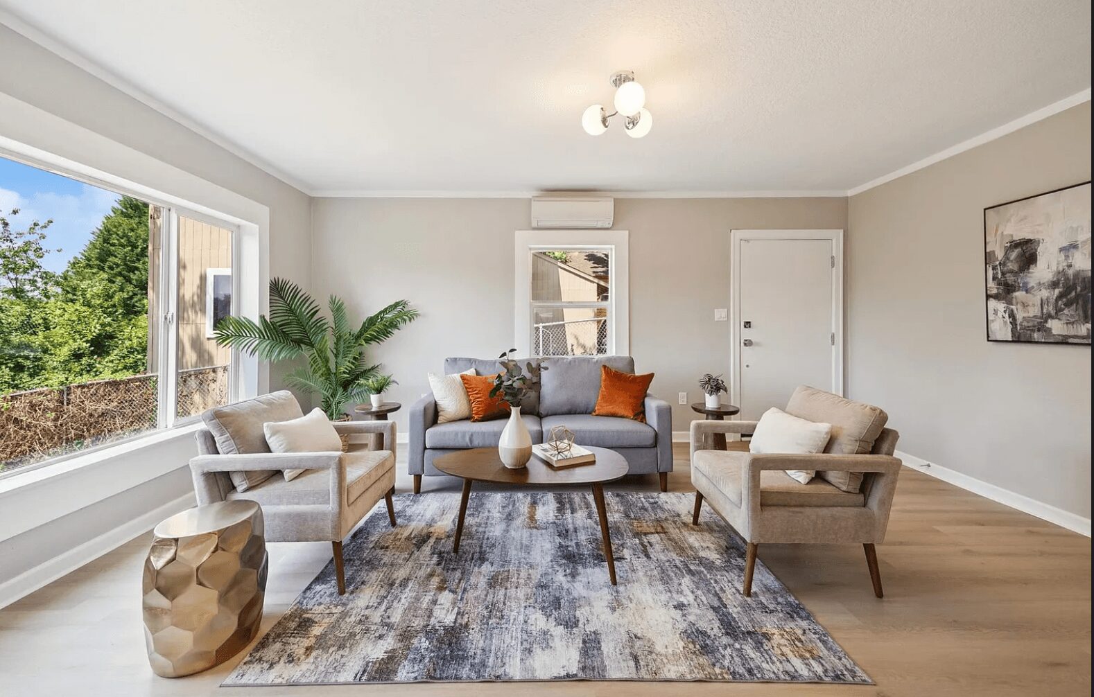 Living room with large window, sofa, two armchairs, potted plant, rug, and wall art.