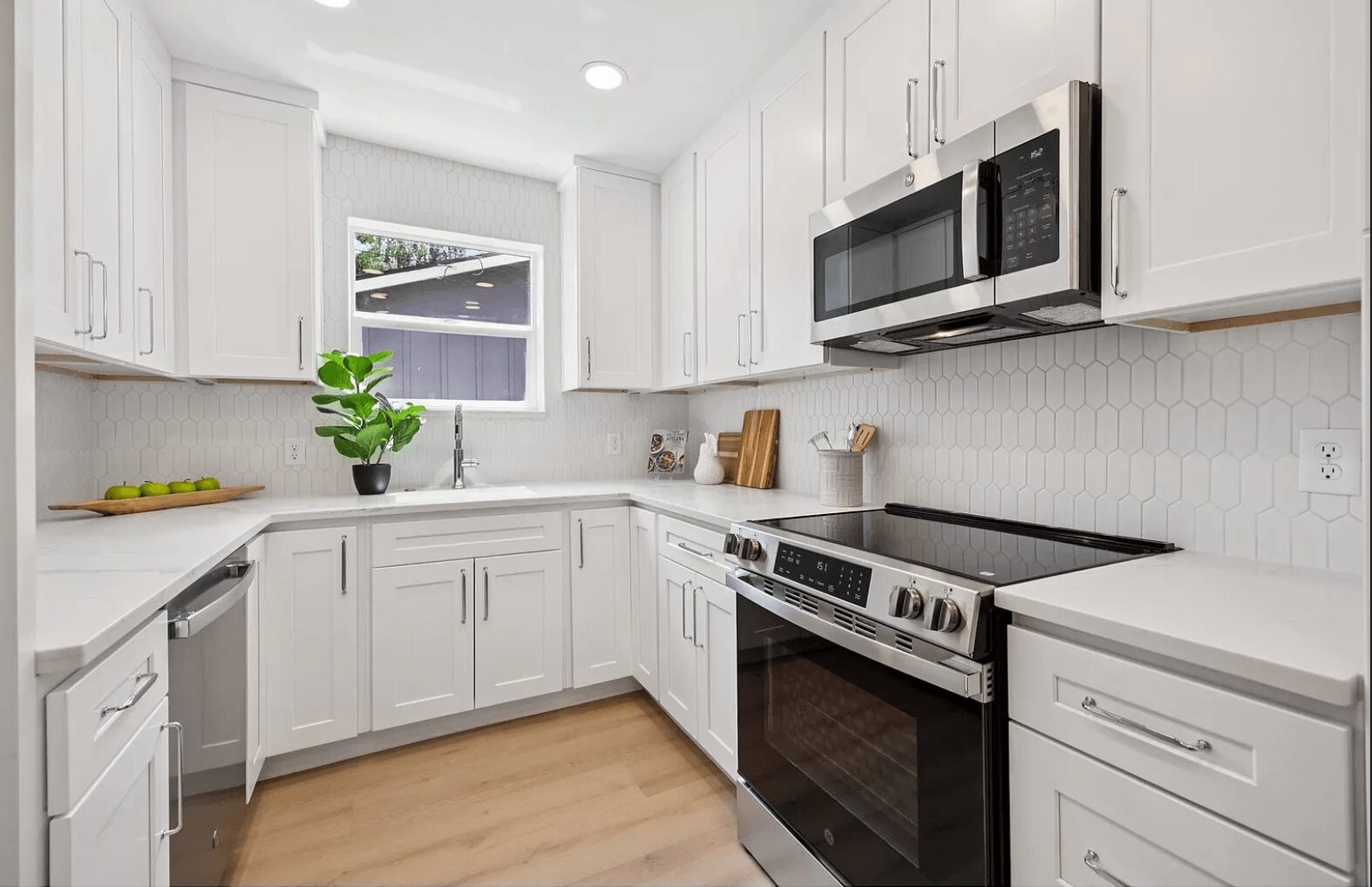 Bright kitchen with white cabinets, stainless steel appliances, a window, and a potted plant on the counter.