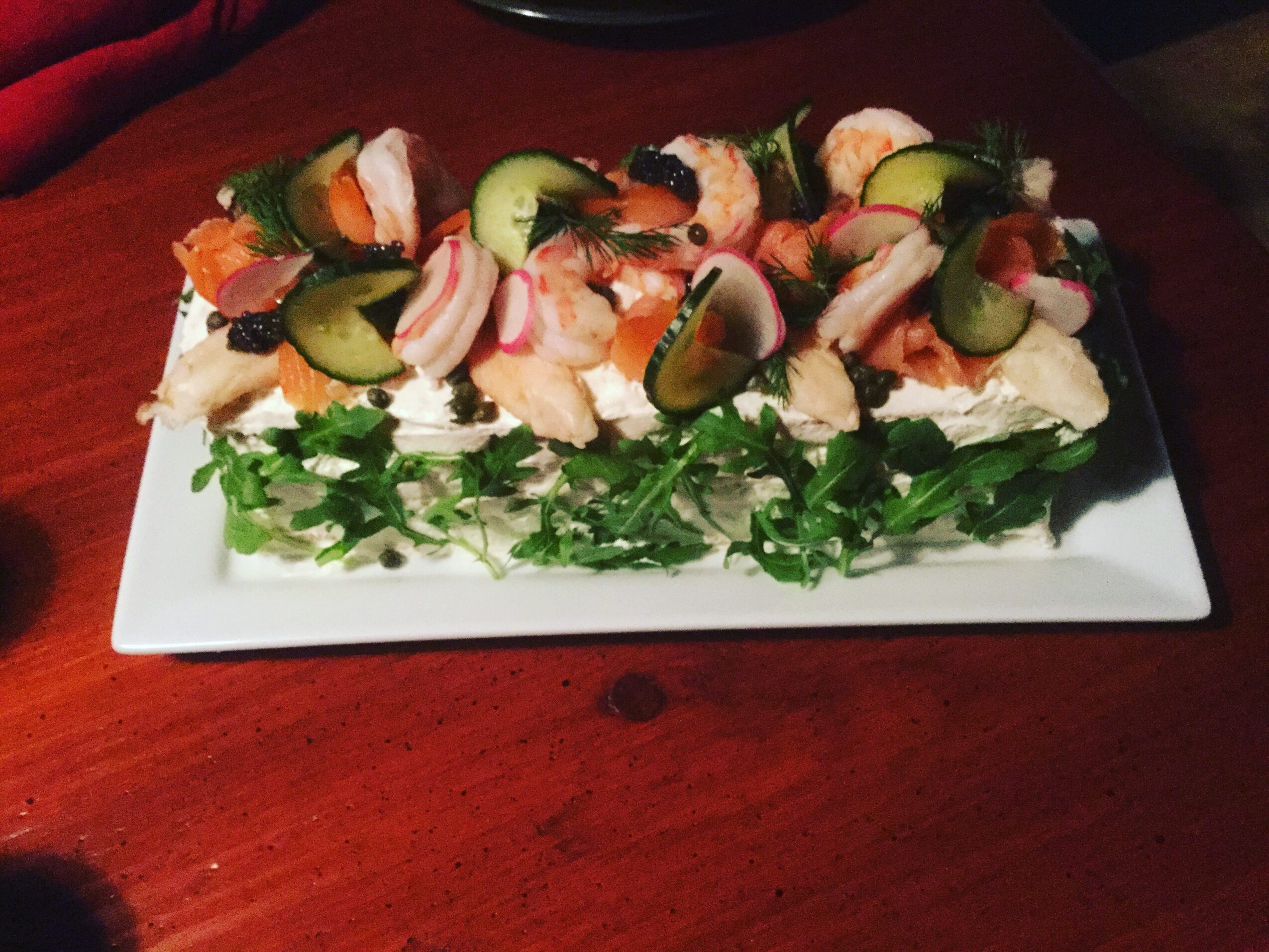A rectangular plate with assorted seafood, vegetables, and greens on a wooden table.