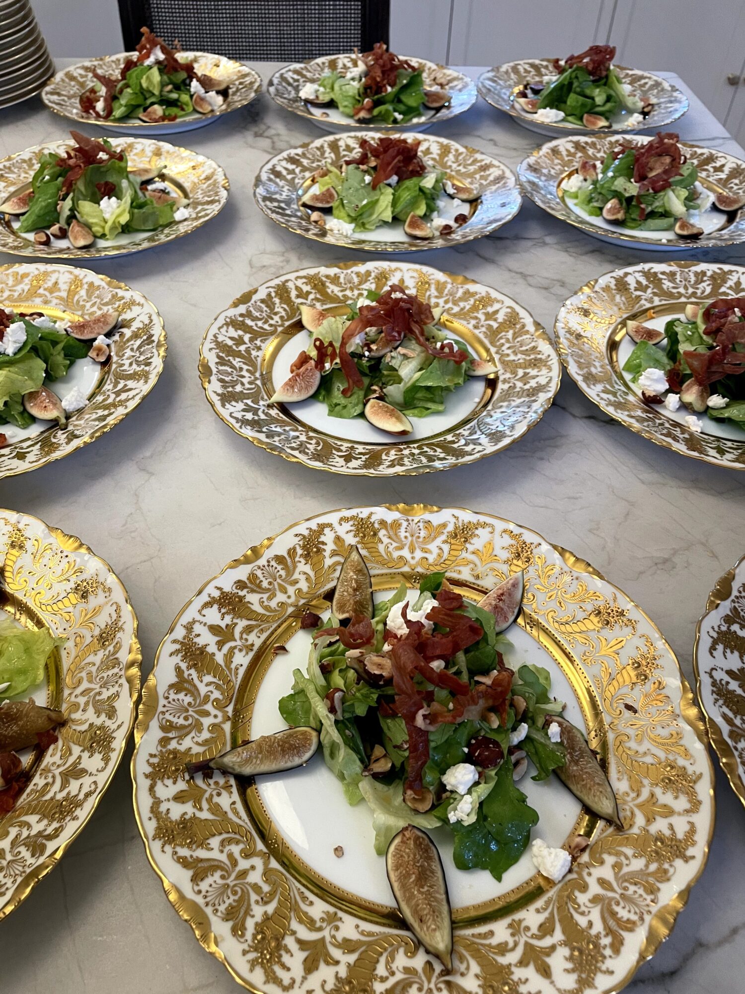 Multiple ornate plates with salad, including greens, sliced vegetables, and garnishes, arranged on a table.