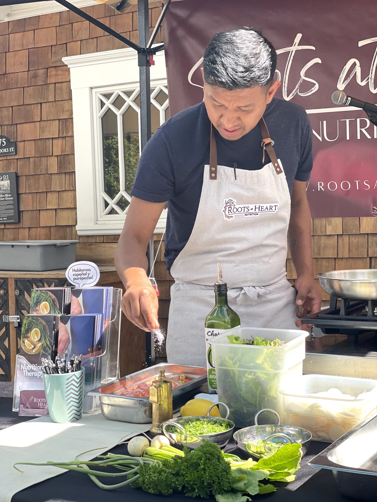 Man wearing apron preparing food outdoors with vegetables and cooking supplies on table.