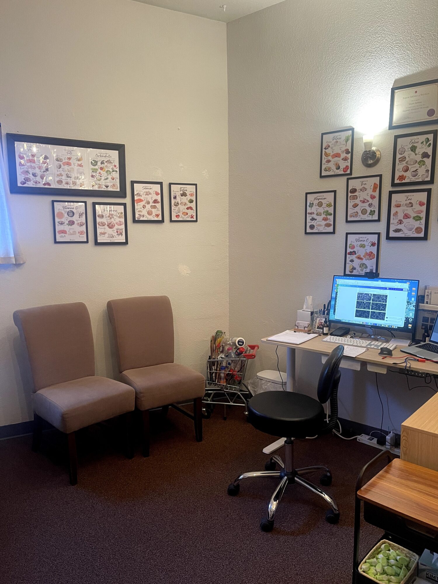 Office corner with two chairs, a desk with a computer, and framed artwork on the walls.