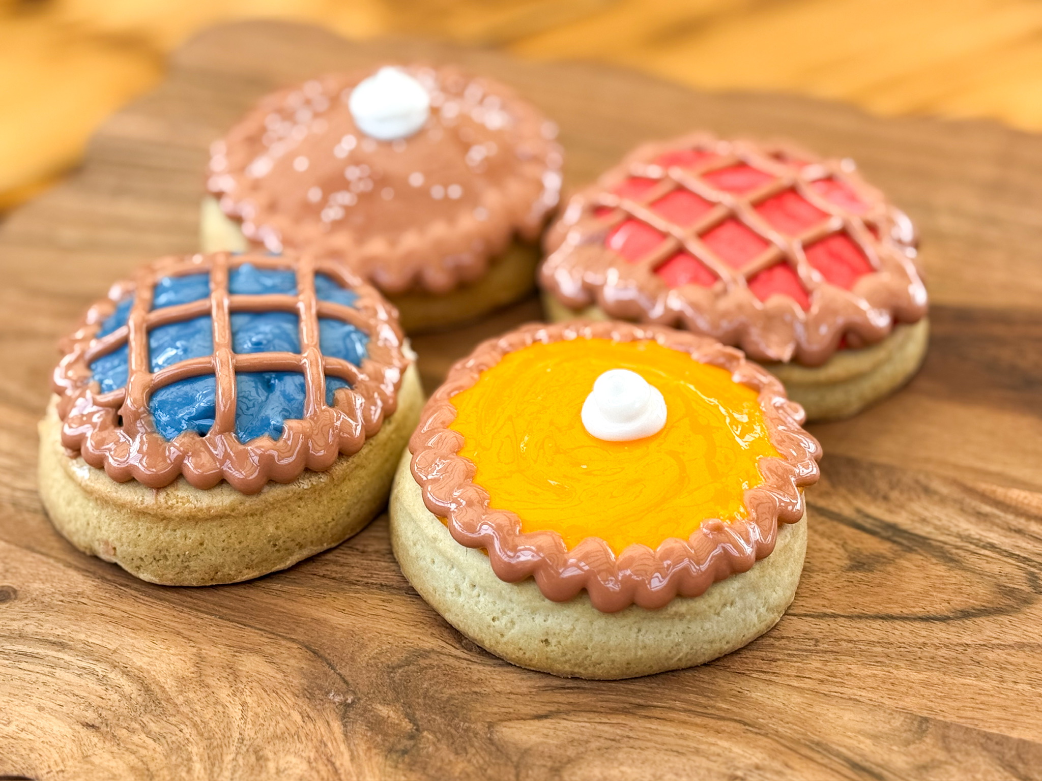 Four decorated cookies on a wooden surface, with colorful icing and patterns, one with a yellow center and white dollop.
