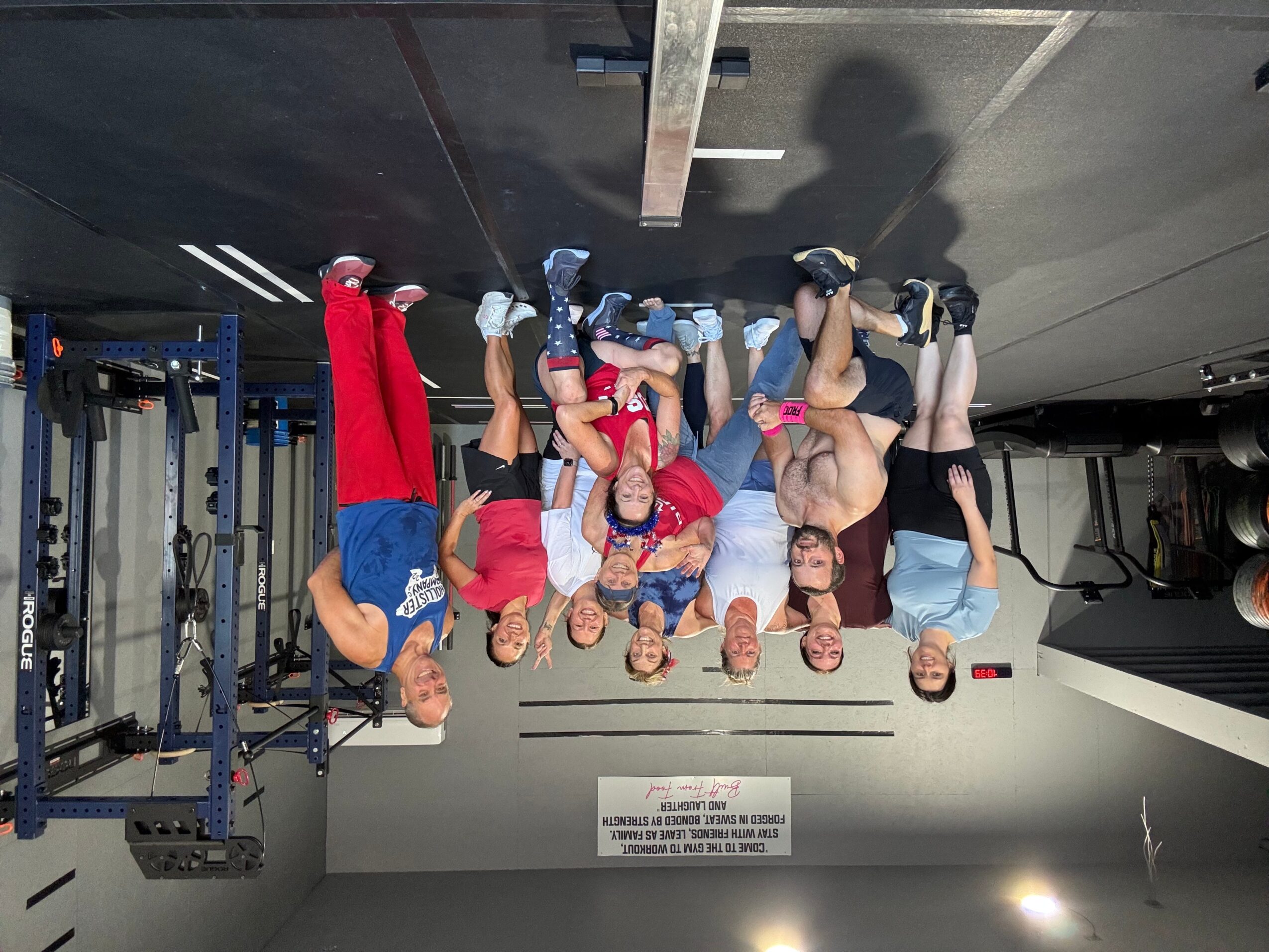 Group of people in workout attire standing in a gym, some with hands on hips, others with arms crossed, facing forward.