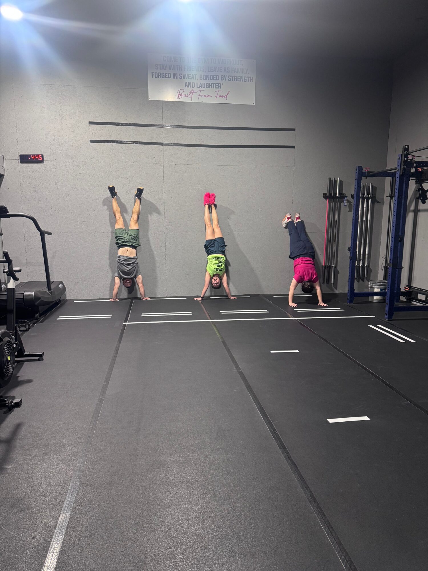 Three children standing on a gym floor, with gym equipment and a wall in the background.