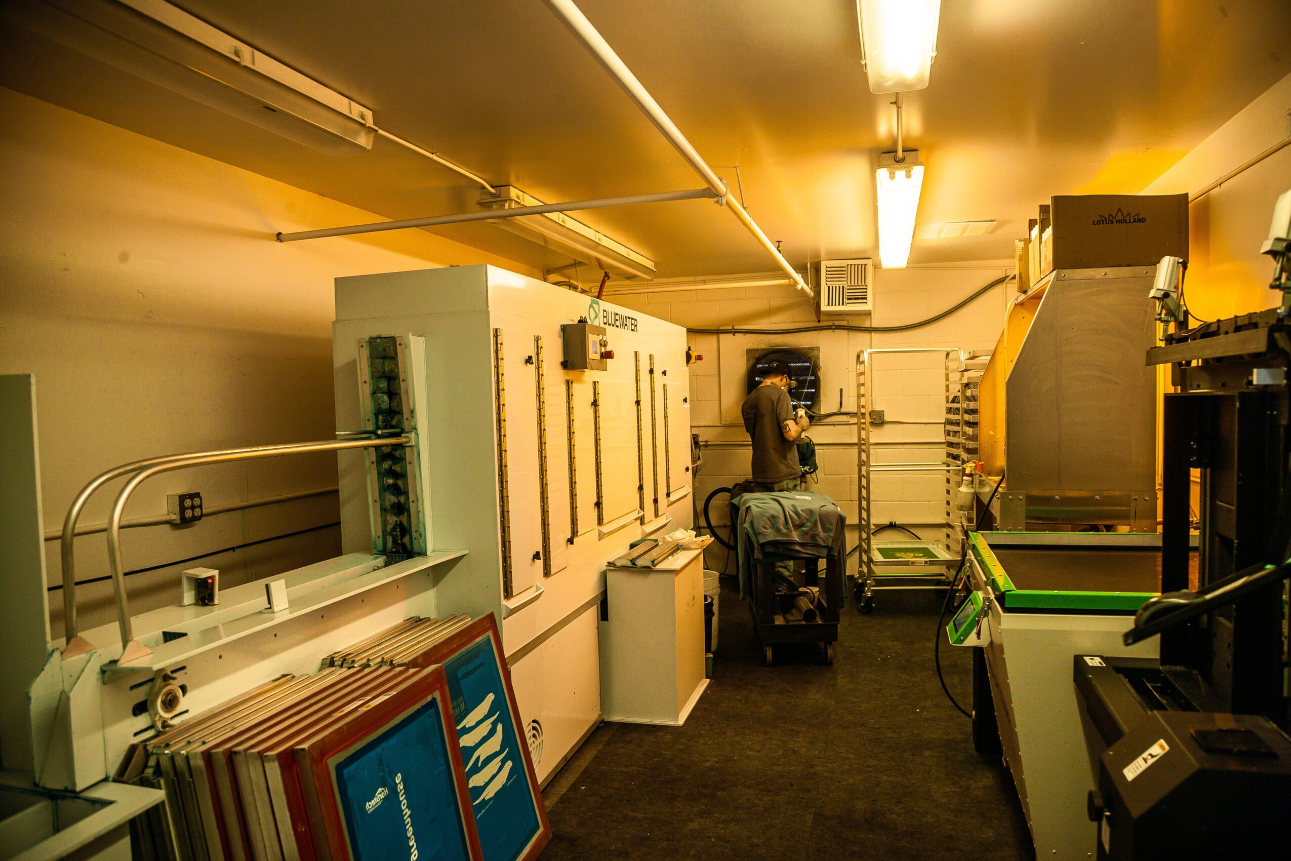 Person working in a room with electrical panels and equipment, carrying a suitcase, with various tools and supplies around.