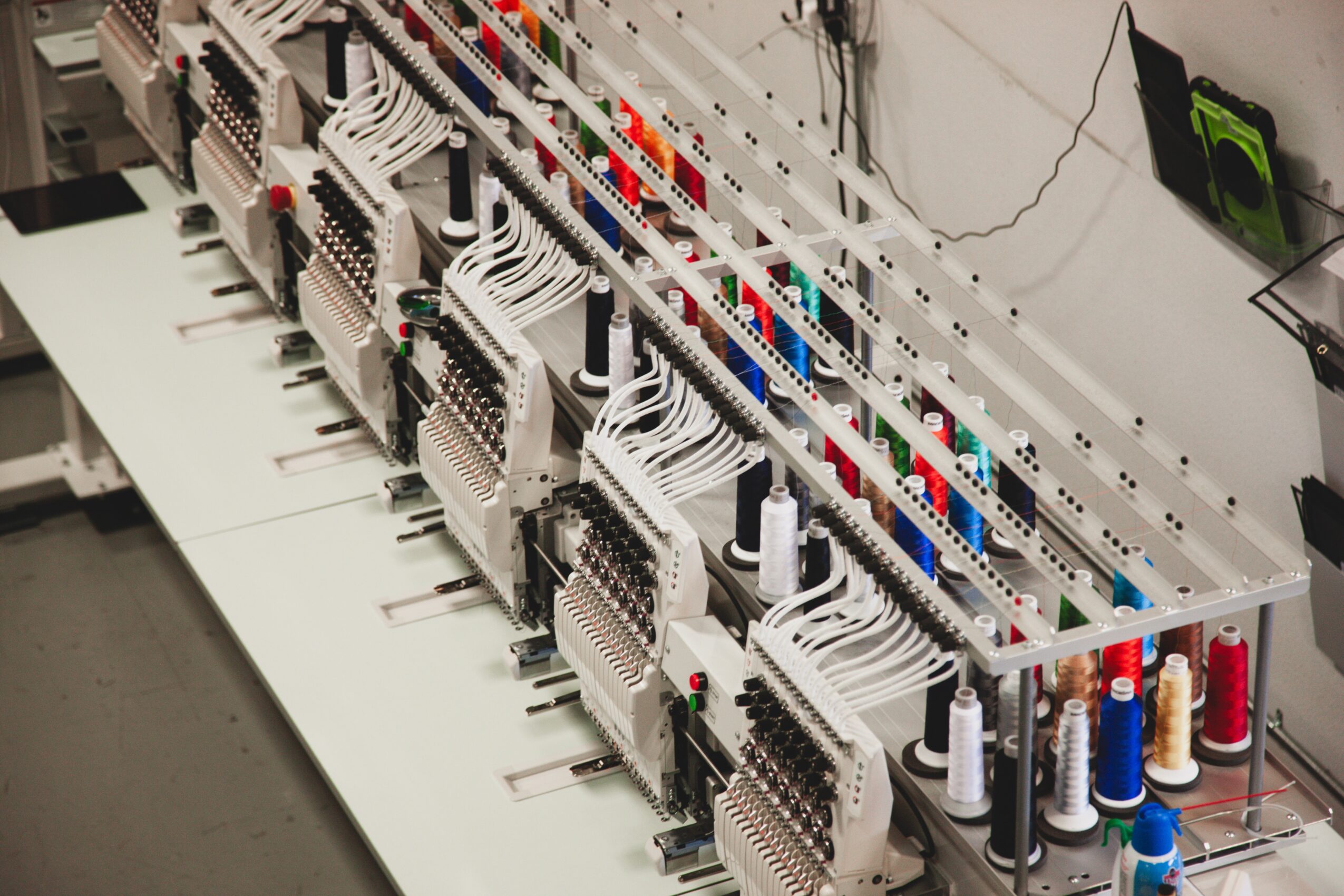 Electrical wiring and components organized on a white panel with multiple spools of thread or wire below, in a workshop or lab.