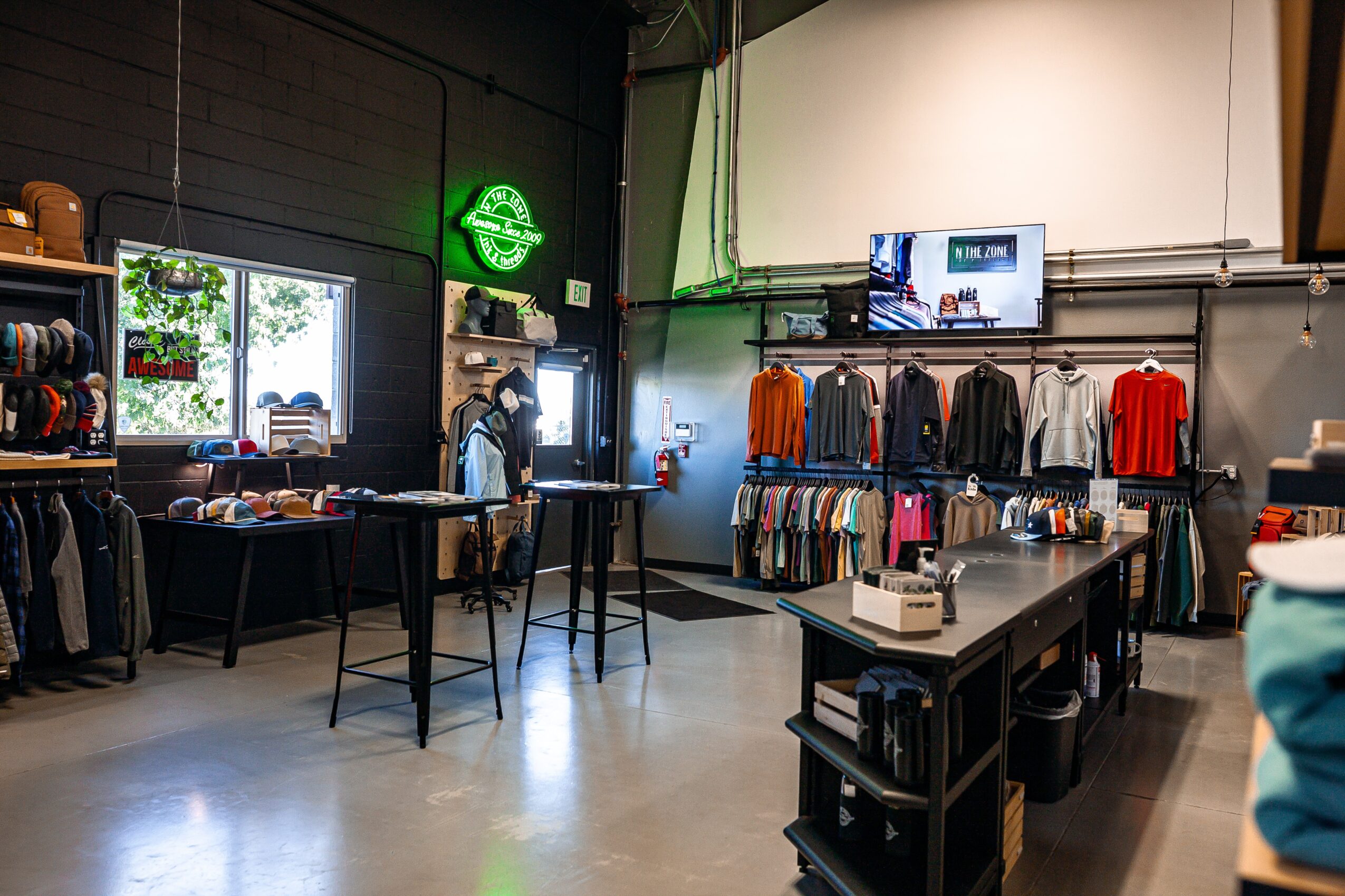 Clothing store interior with racks of clothes, a table, and a television screen on the wall.