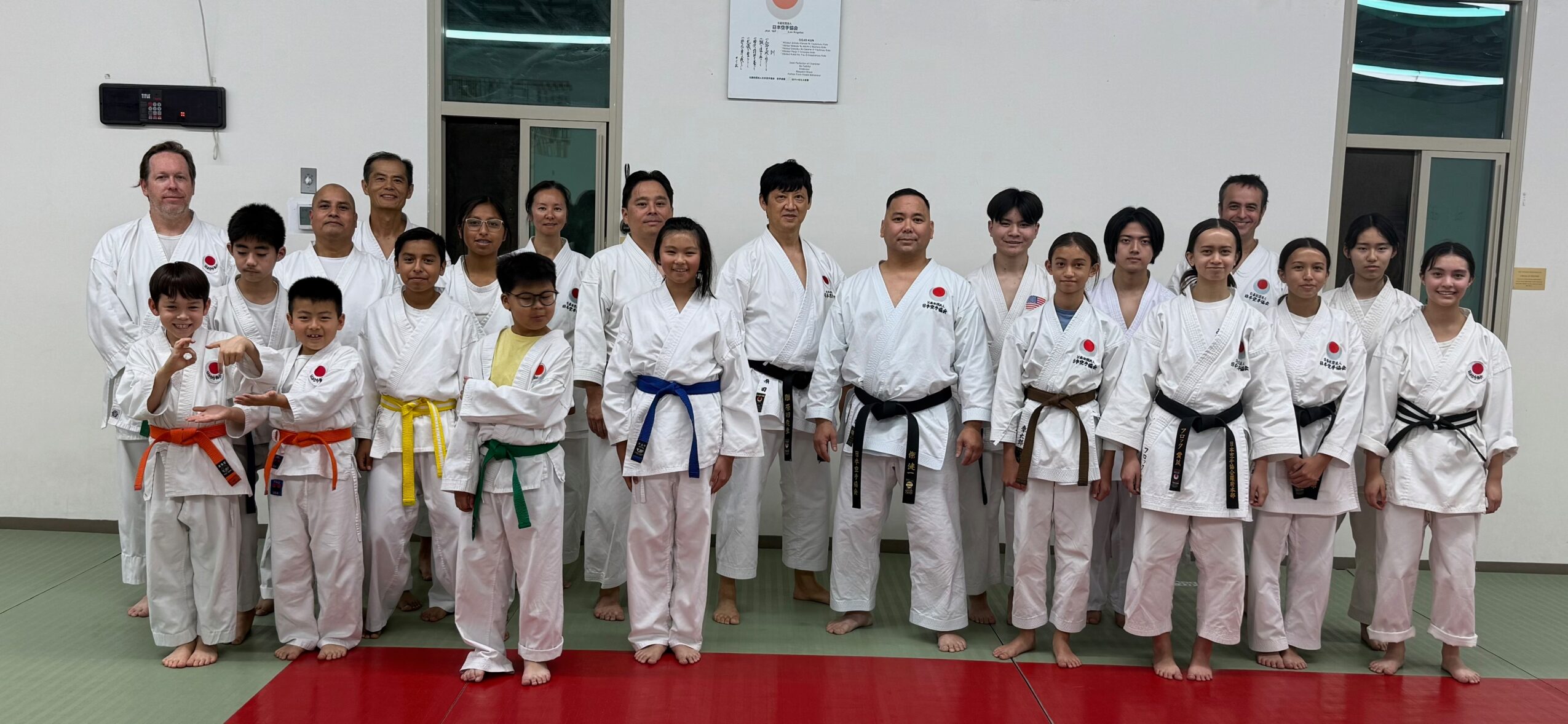 Group of martial arts students and instructor in uniform, standing in dojo, posing for photo.