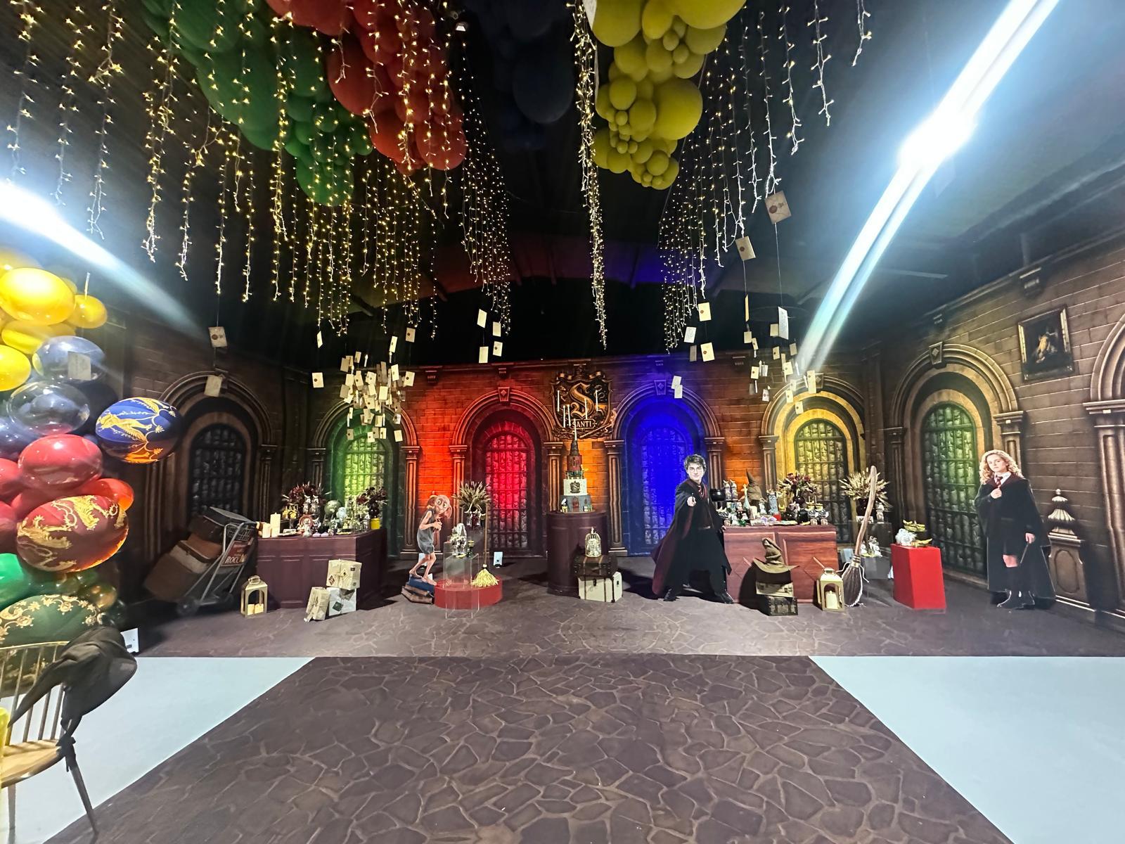 Decorated indoor space with colorful balloons, hanging decorations, and people standing near tables, with a backdrop resembling a castle or palace.
